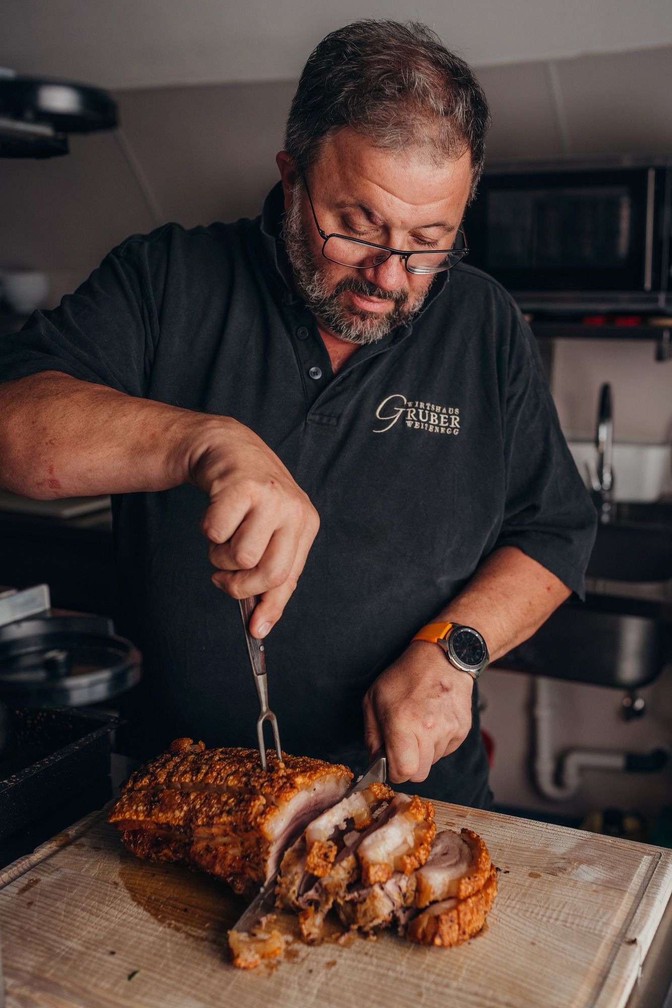 Mann schneidet knusprigen Schweinebraten in einer Küche.