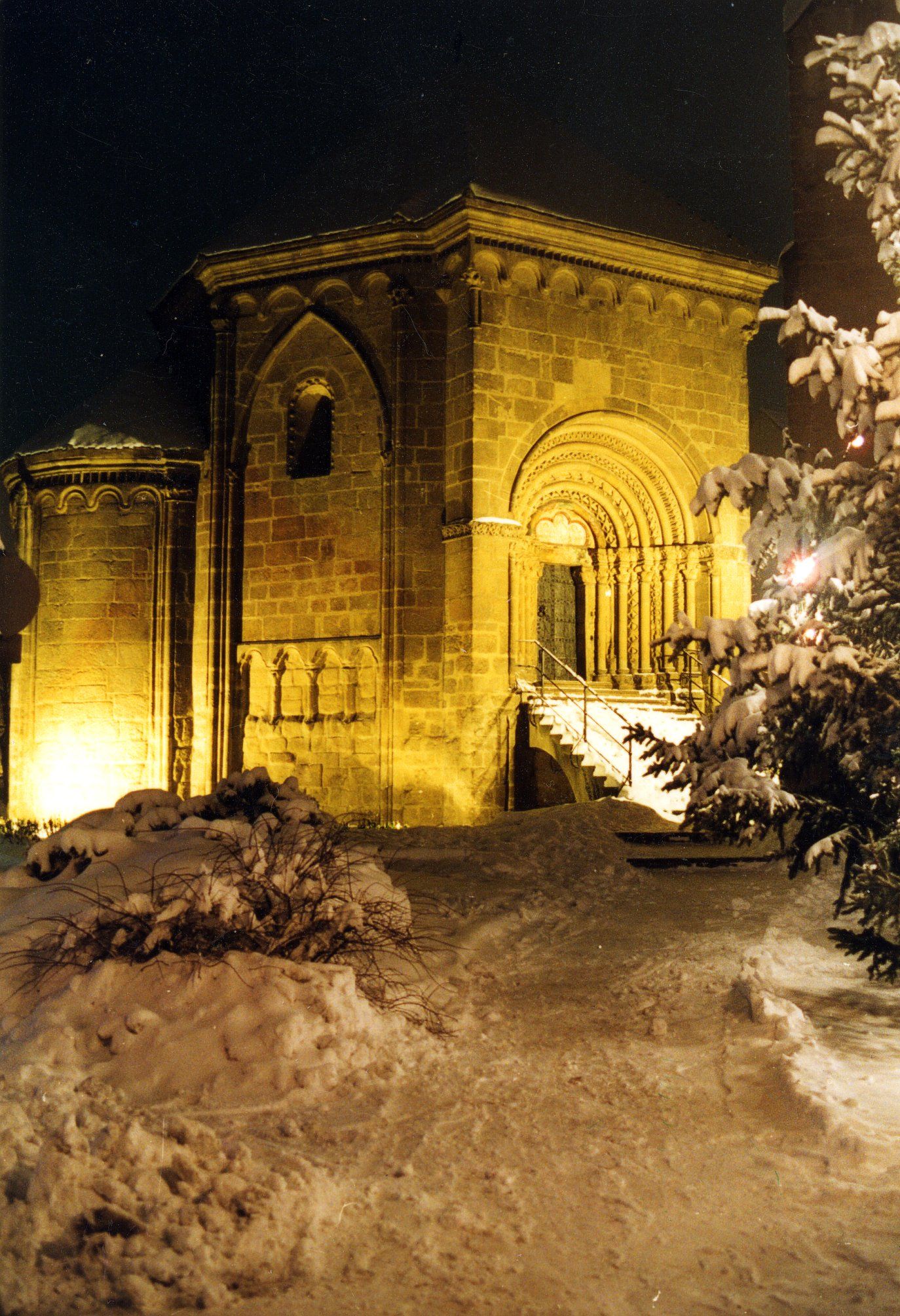 Der Tullner Karner bei Nacht, umgeben von Schnee, mit beleuchteter romanischer Architektur.
