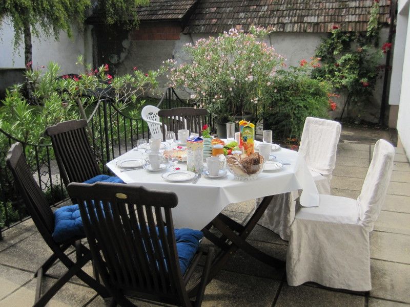 Ein gedeckter Tisch auf einer Terrasse mit Stühlen, umgeben von Pflanzen.