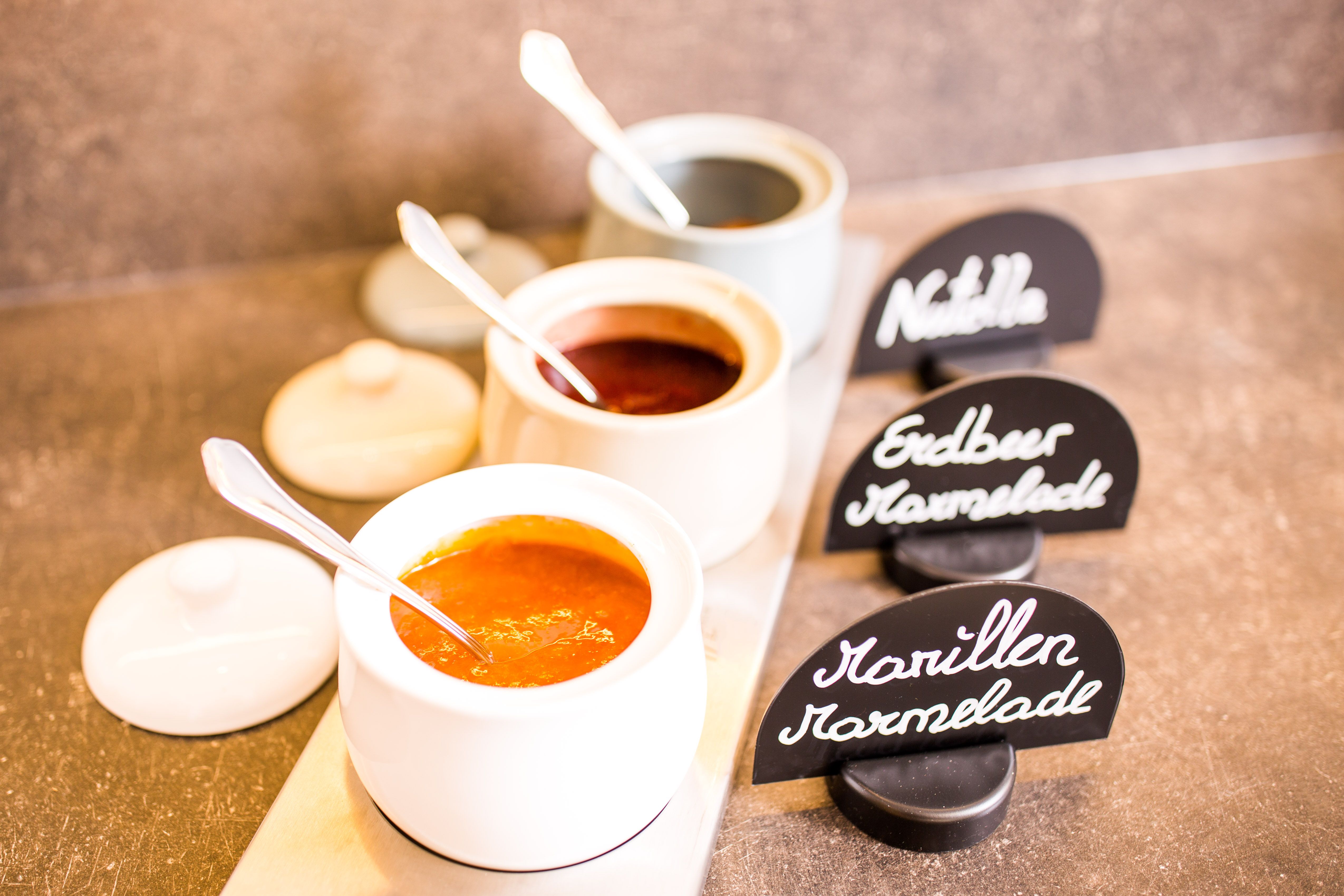 Drei Schalen mit Marmelade und Nutella, beschriftet mit "Marillen Marmelade", "Erdbeer Marmelade" und "Nutella".