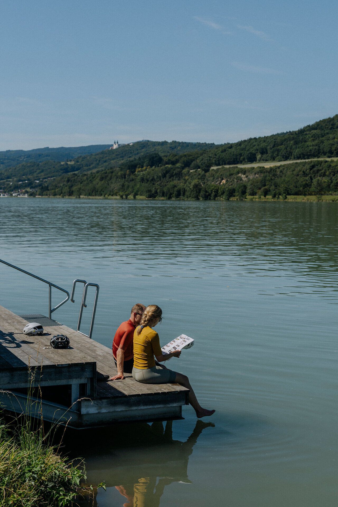 2 Radfahrer sitzen an einem Donausteg und betrachten die Schatzkarte Nibelungengau 
