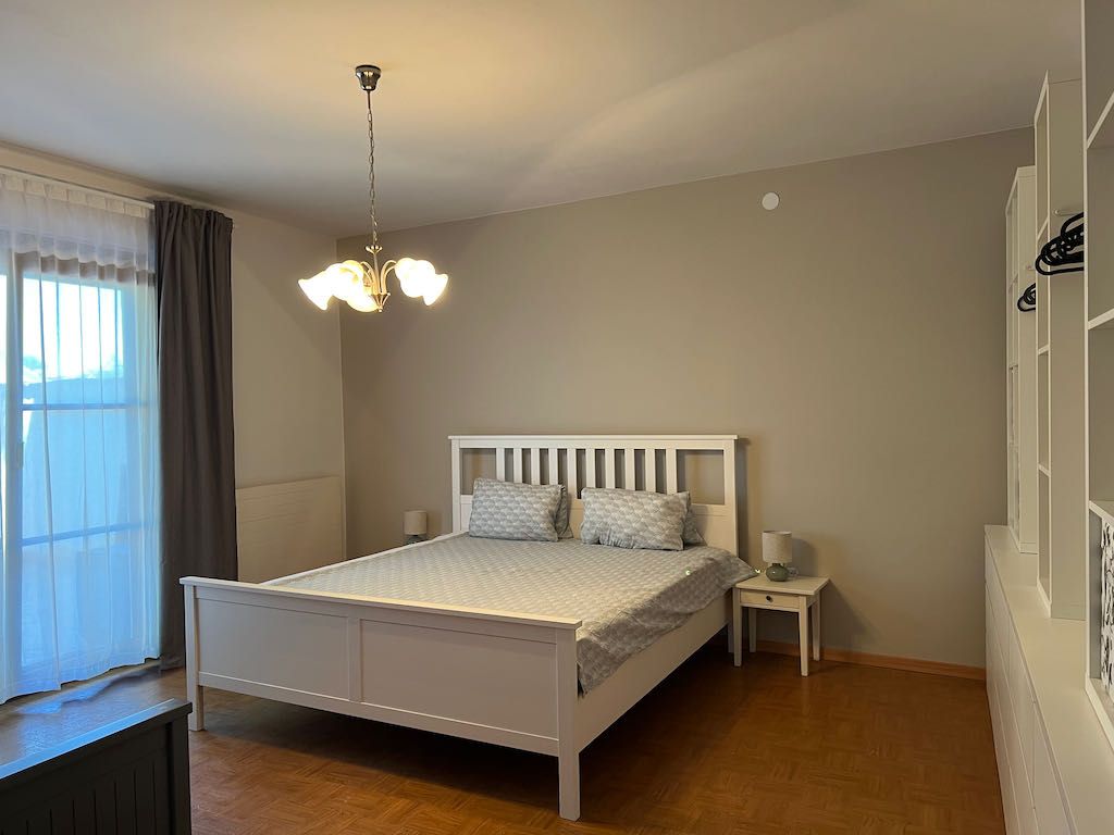 Schlafzimmer mit weißem Bett, Nachttisch und Kleiderschrank.