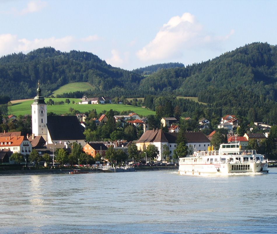 Town of Grein with church and ship on the Danube, surrounded by hills.
