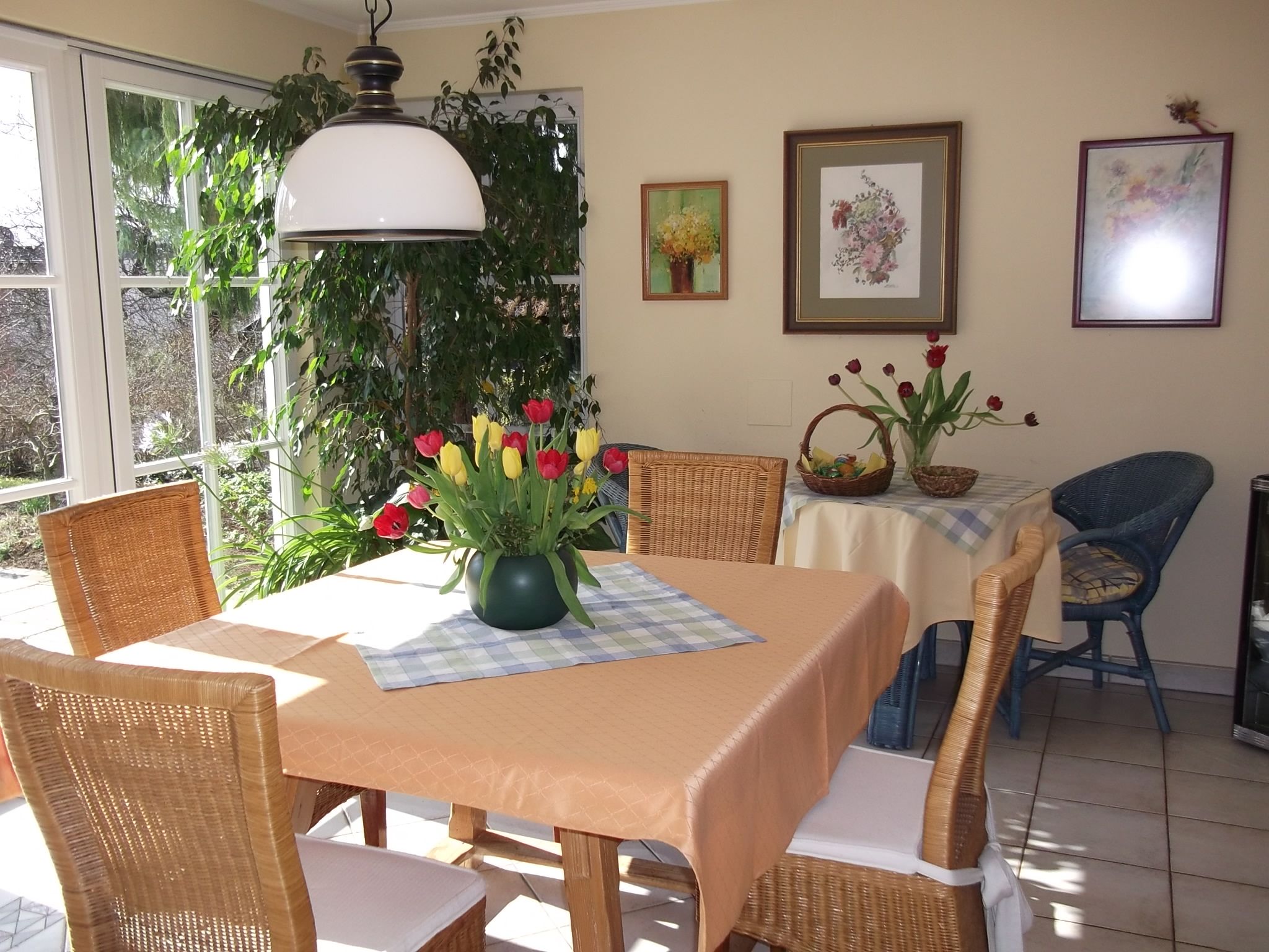 Ein gemütlicher Essbereich mit einem Tisch, auf dem ein Blumenstrauß steht, umgeben von Korbstühlen und dekorativen Bildern an der Wand.