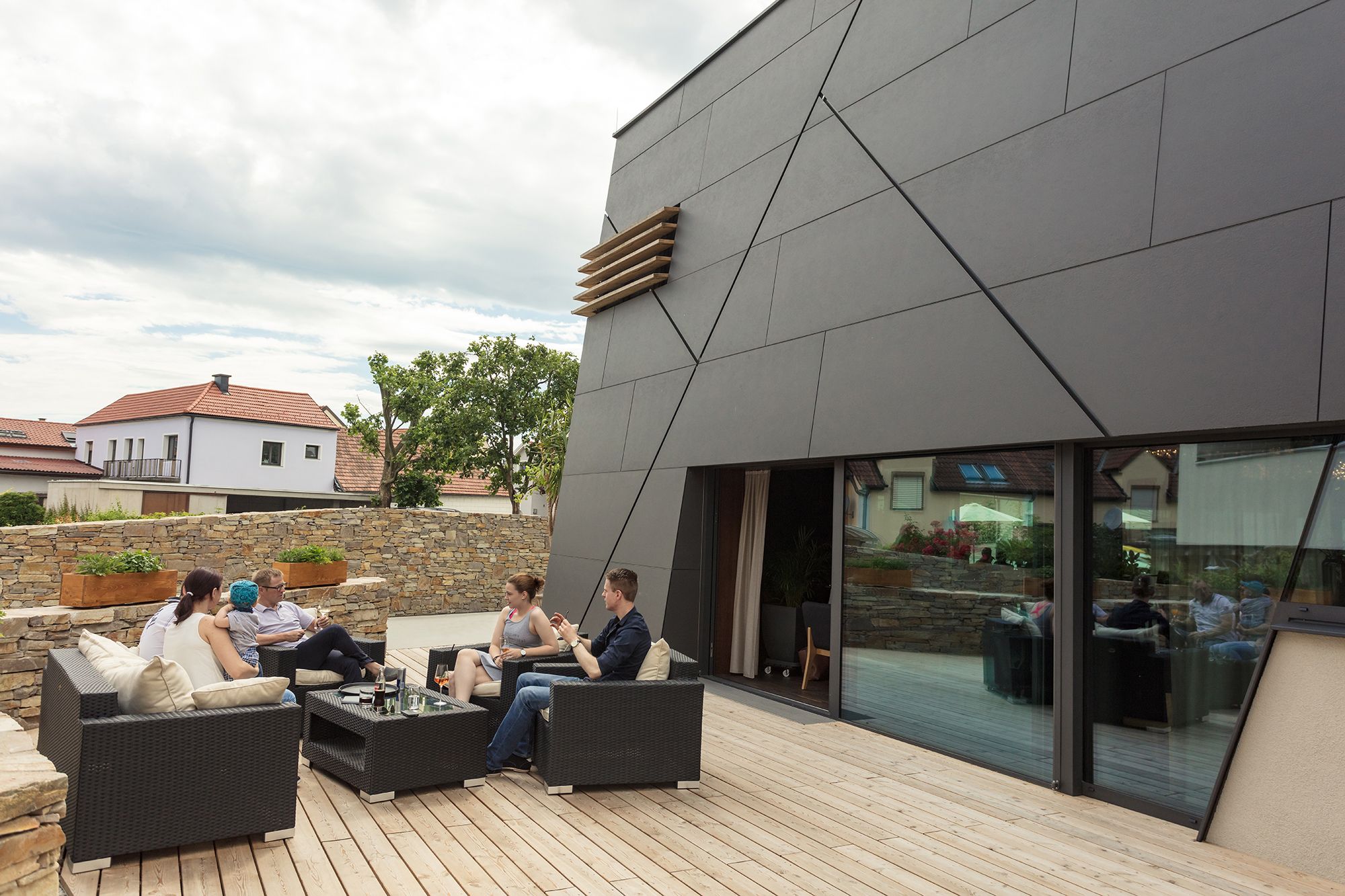 Menschen sitzen auf einer Terrasse vor einem modernen Gebäude.