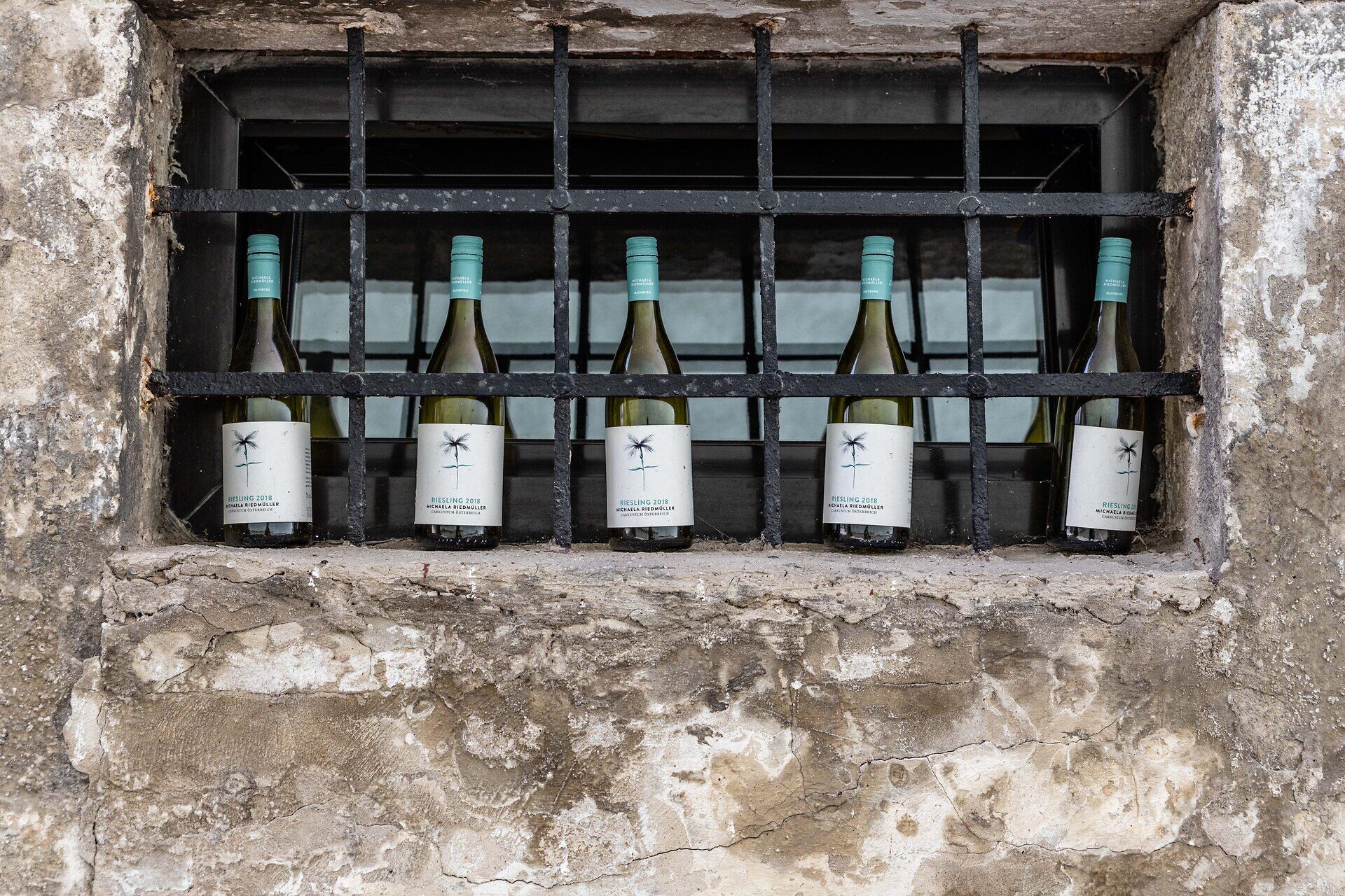 Weinflaschen stehen vor einem alten Kellerfenster mit Eisenverstrebung.