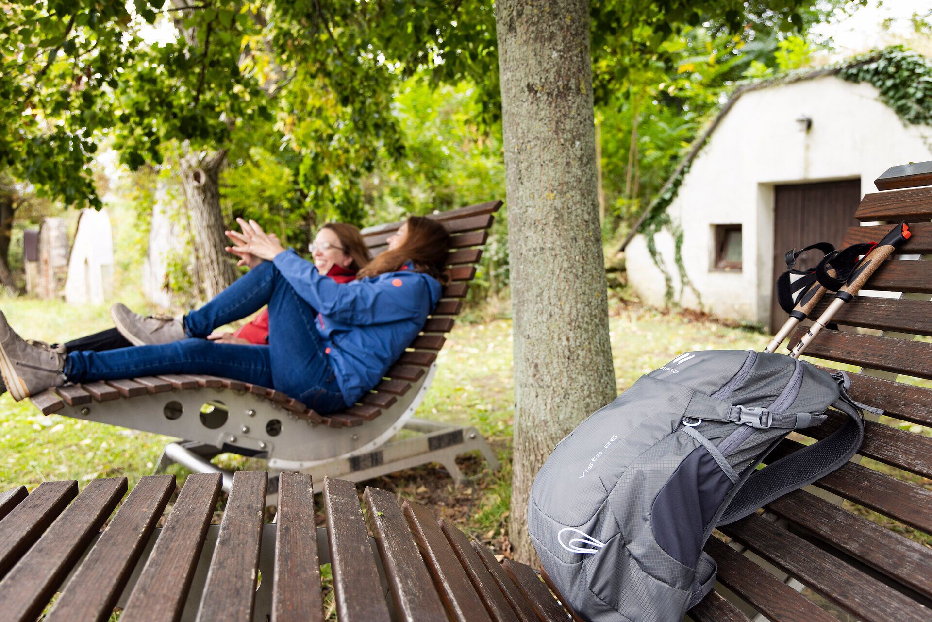 Zwei Frauen auf einer Holzliege, ein Wanderrucksack und im Hintergrund alte Weinkeller. 