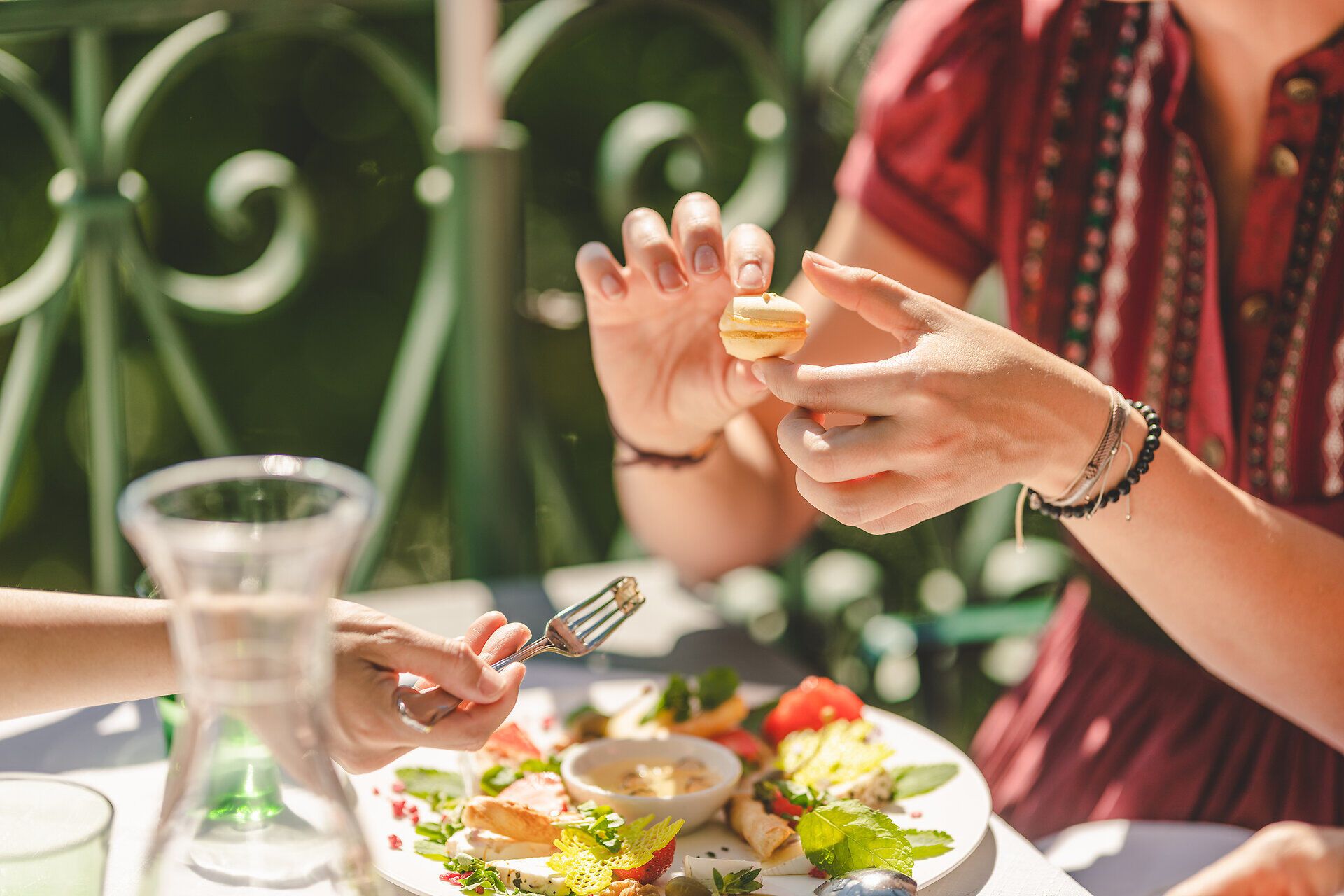 Zwei Damenhände halten einen Bissen von einem schön angerichteten Teller.