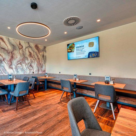 Modern restaurant with wooden floor, gray chairs and a large screen on the wall.