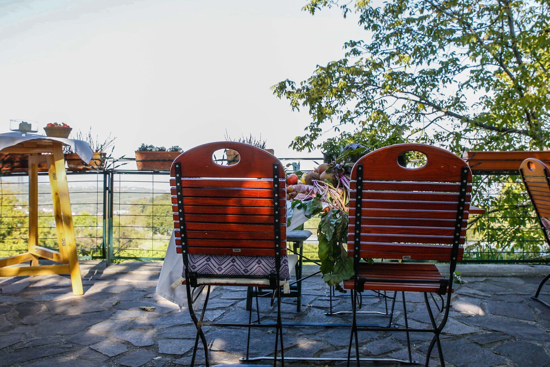 Genießen Sie die Ruhe und den Blick auf die sanften Hügel, während die Sonne sanft durch die Blätter der Bäume scheint. Die rustikalen Stühle laden dazu ein, Platz zu nehmen und die frische Luft zu atmen, während der Duft von blühenden Pflanzen die Sinne betört.