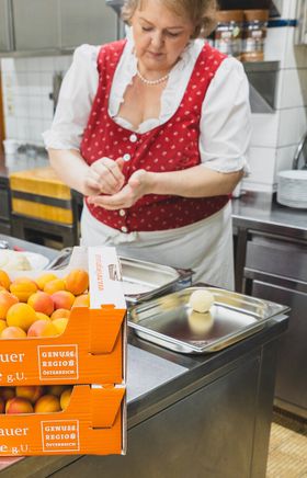 In einer einladenden Küche werden frische Marillen zu köstlichen Knödeln verarbeitet. Der Duft von reifen Früchten und die Vorfreude auf den Sommer verleihen der Szene eine besondere Atmosphäre. Hier wird Tradition mit Leidenschaft gelebt.