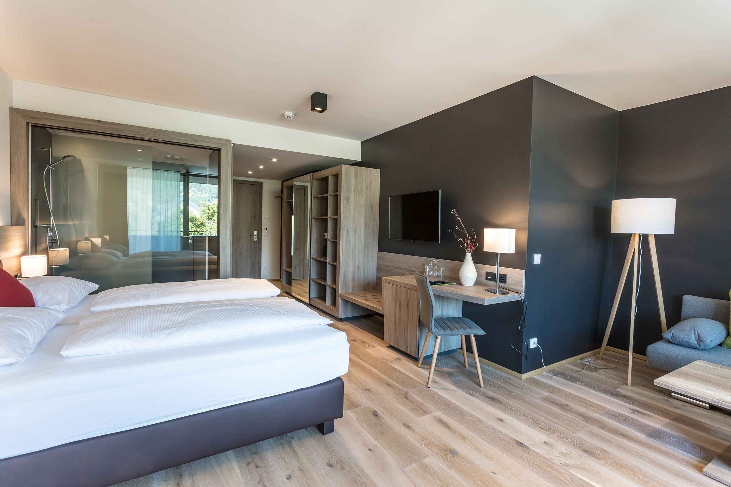 Modernes Hotelzimmer mit Doppelbett, Schreibtisch, Fernseher und Glasdusche.