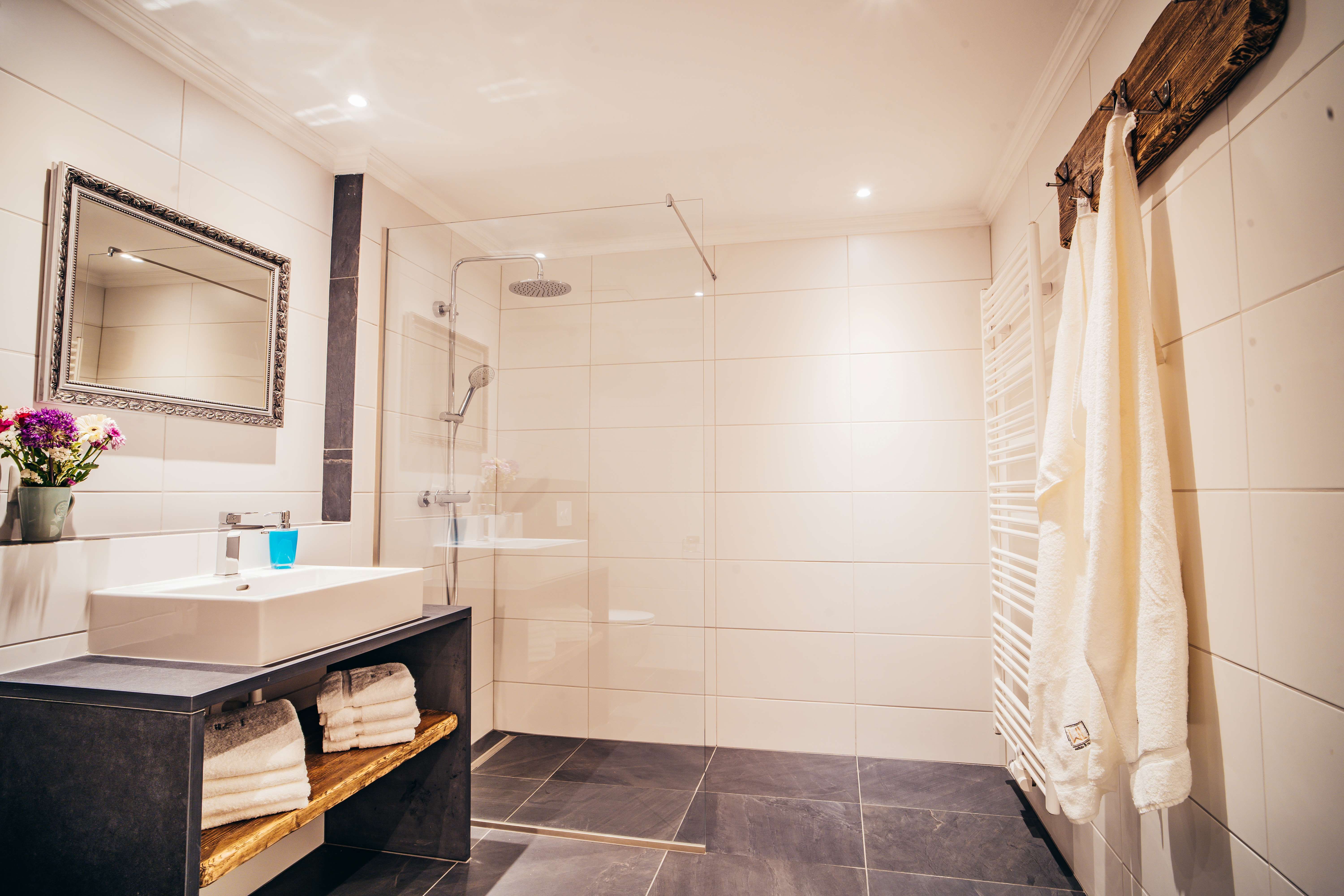 Modernes Badezimmer mit großer Dusche, Waschbecken, Spiegel und Handtüchern.