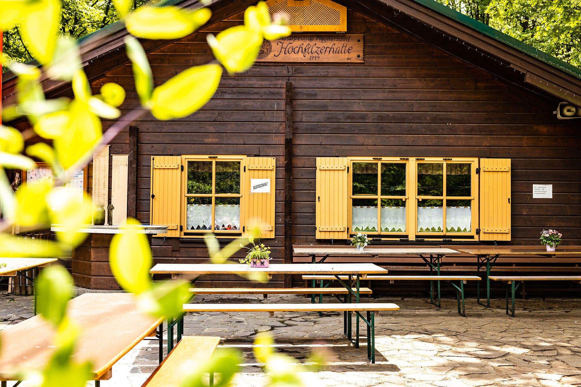 Holzhütte "Hochfilzerhütte" mit Tischen und Bänken davor. 