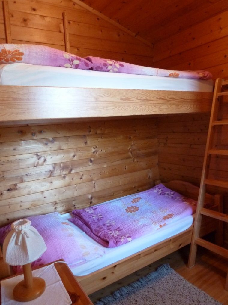 Innenansicht eines Holzferienhauses mit Etagenbett und lila Bettwäsche.