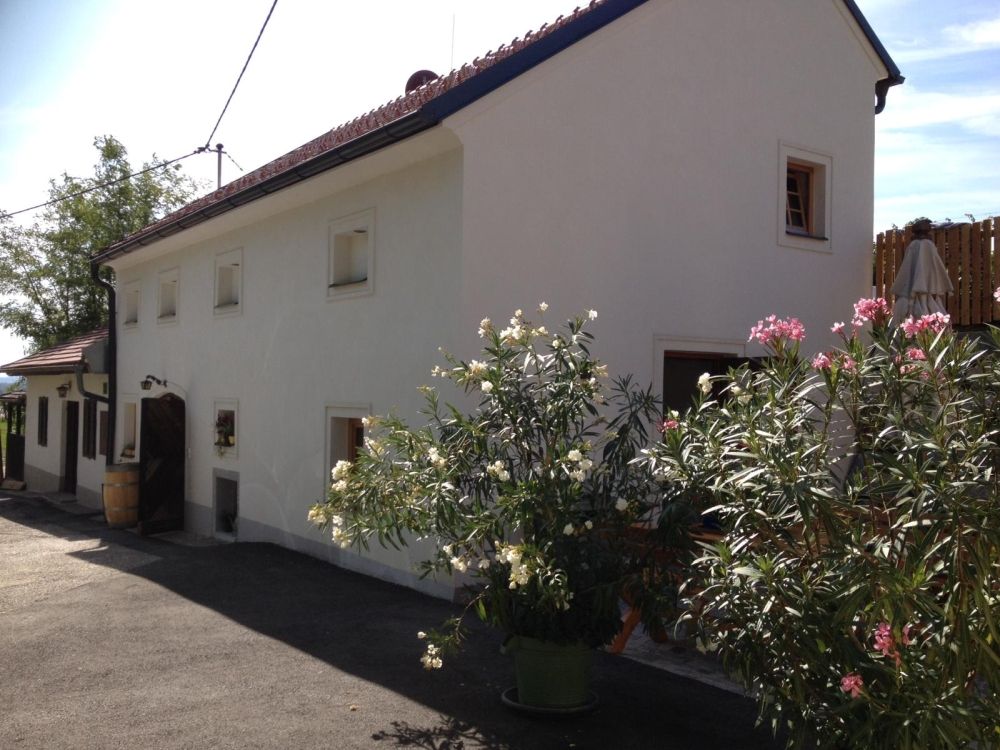 Weißes Gebäude mit roten Dachziegeln und blühenden Oleanderbüschen davor.