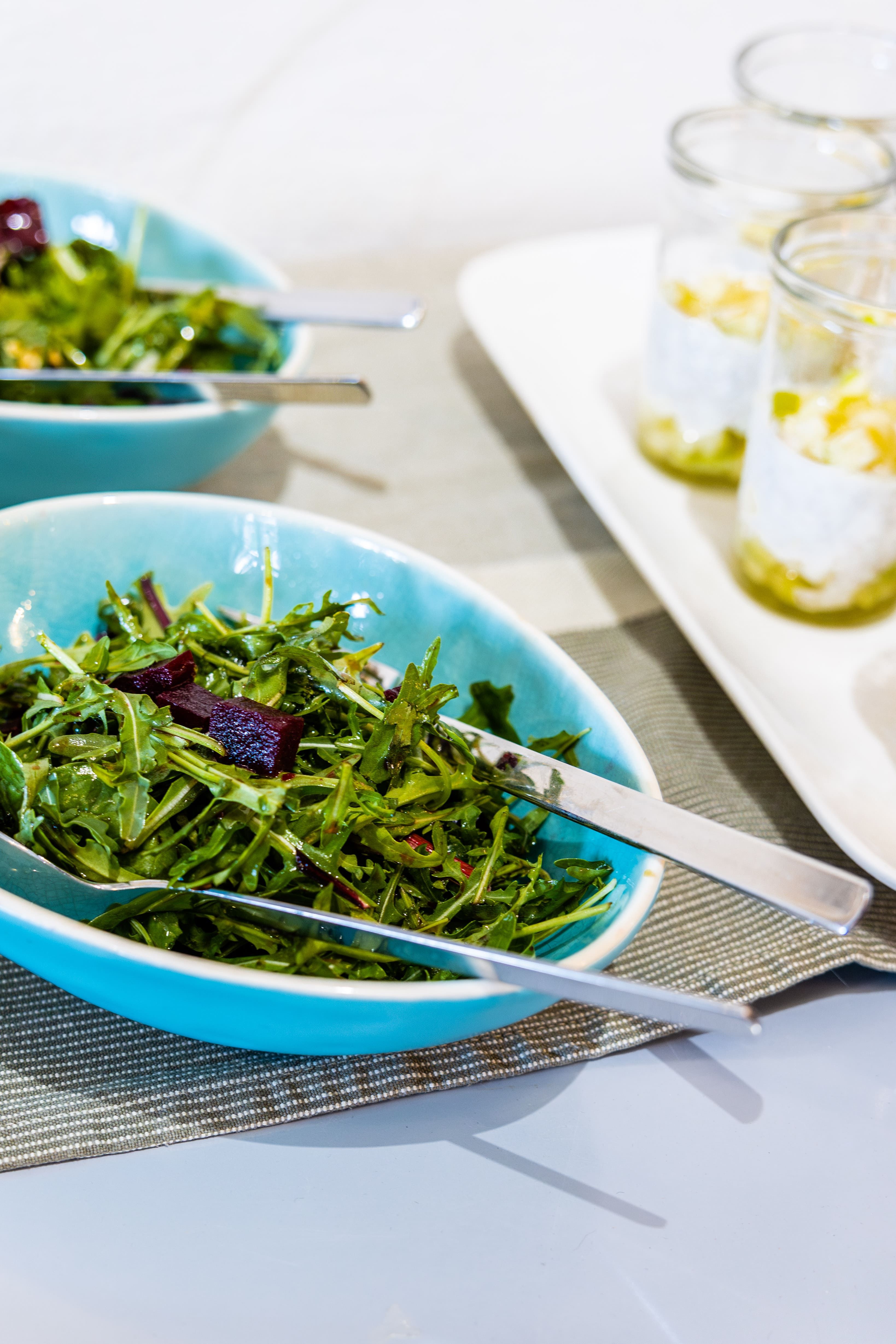 Schüssel mit Rucola-Salat und Besteck auf einem Tisch.