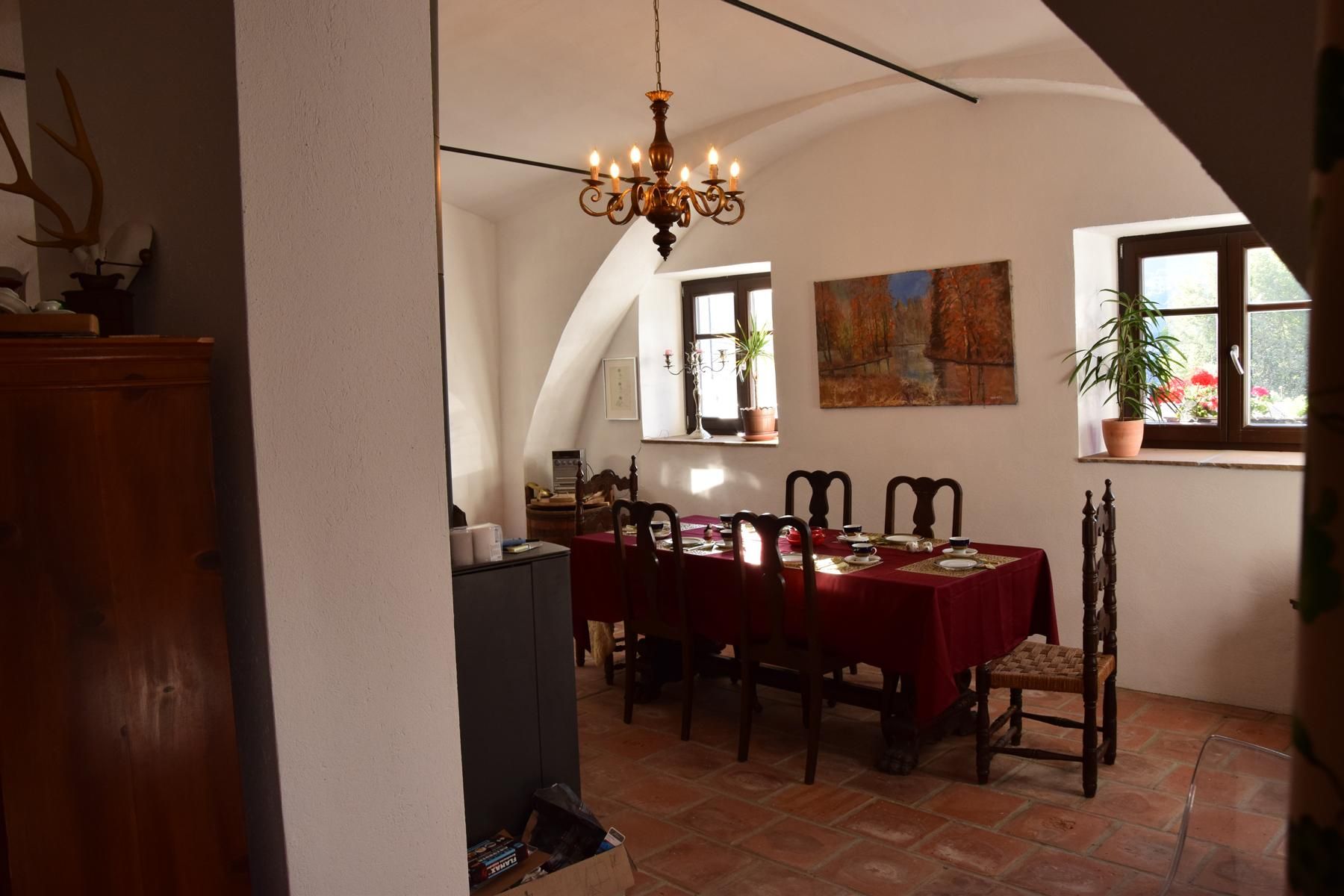 Ein Esszimmer mit einem Tisch, der mit einer roten Tischdecke gedeckt ist. An der Wand hängt ein Gemälde, und ein Kronleuchter hängt von der Decke.