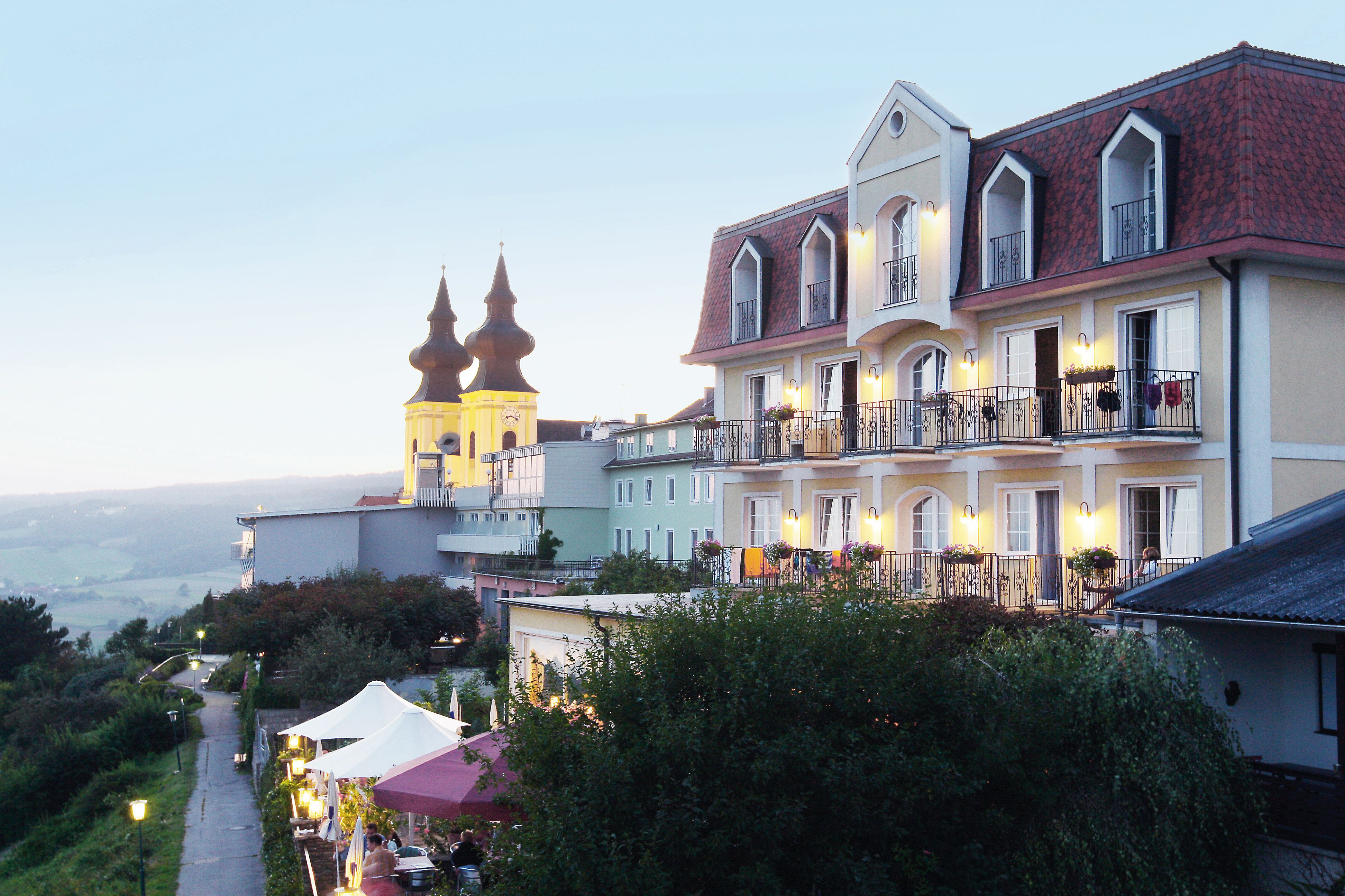 Ein Hotel mit Balkonen und einer Kirche im Hintergrund bei Dämmerung.