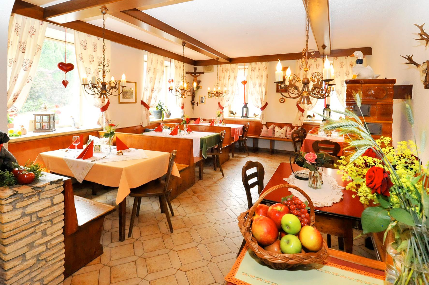 Cozy restaurant area with wooden furniture, decorative curtains and flower arrangements.