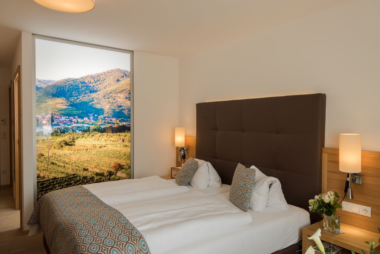 Modernes Hotelzimmer mit Doppelbett, dekorativen Kissen und großem Landschaftsbild an der Wand.