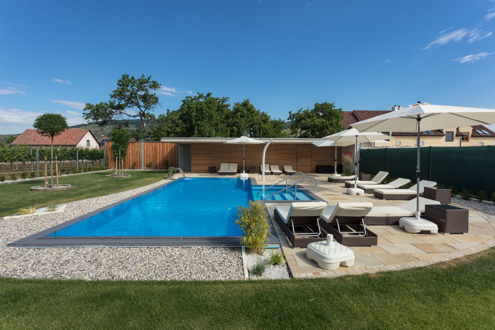 Moderner Außenpool mit Liegestühlen und Sonnenschirmen in einem gepflegten Garten.