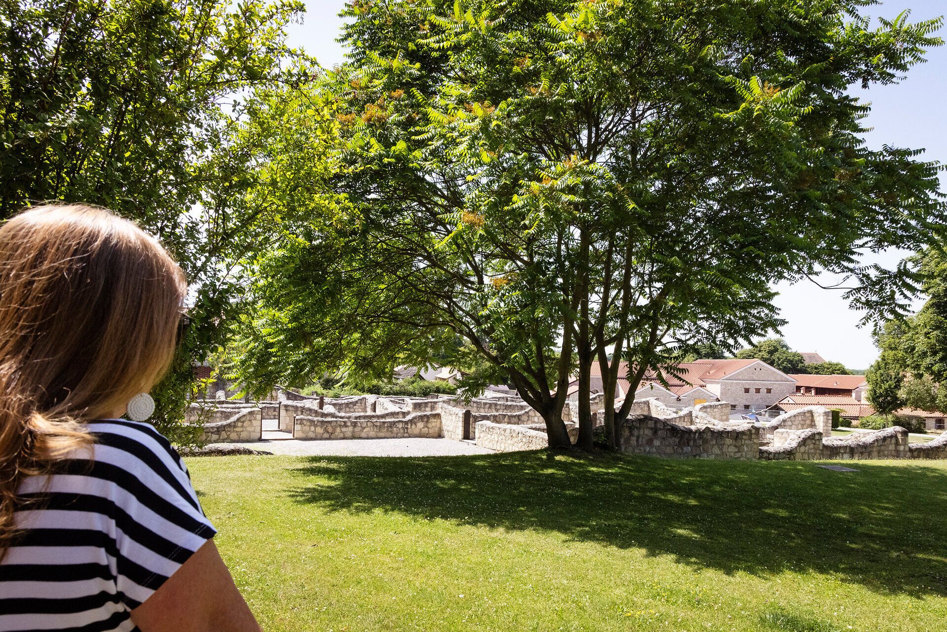 Frau blickt auf das Gelände der Römerstadt Carnuntum mit Steinhäusern. 