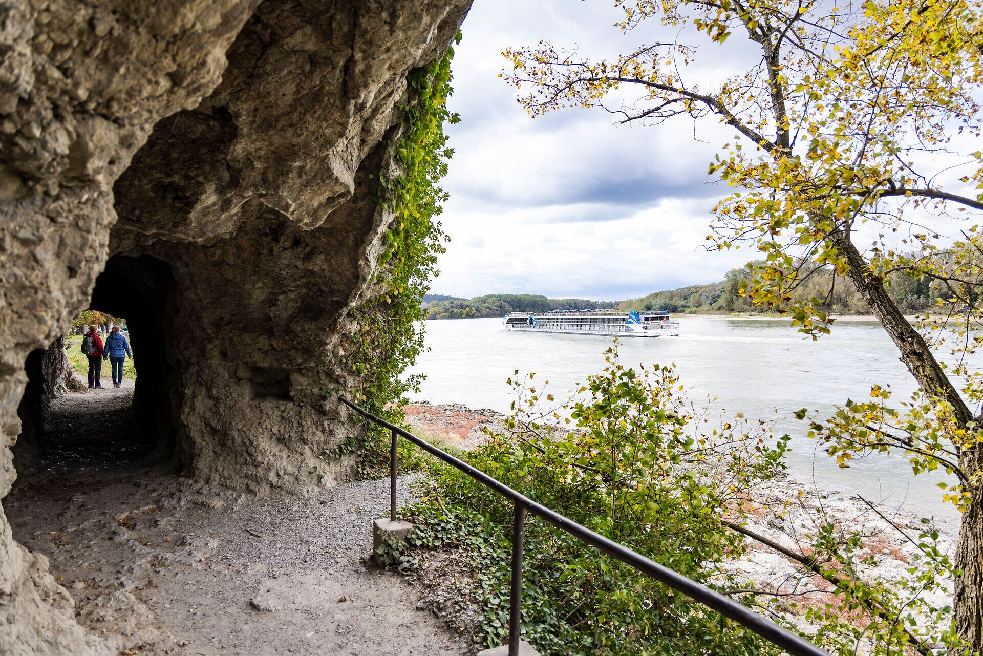 Felsdurchgang auf einem Wanderweg neben der Donau, auf der ein großes Schiff fährt.
