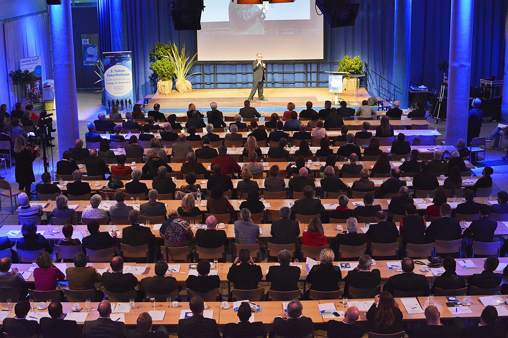 A speaker addresses a large audience in a conference hall.