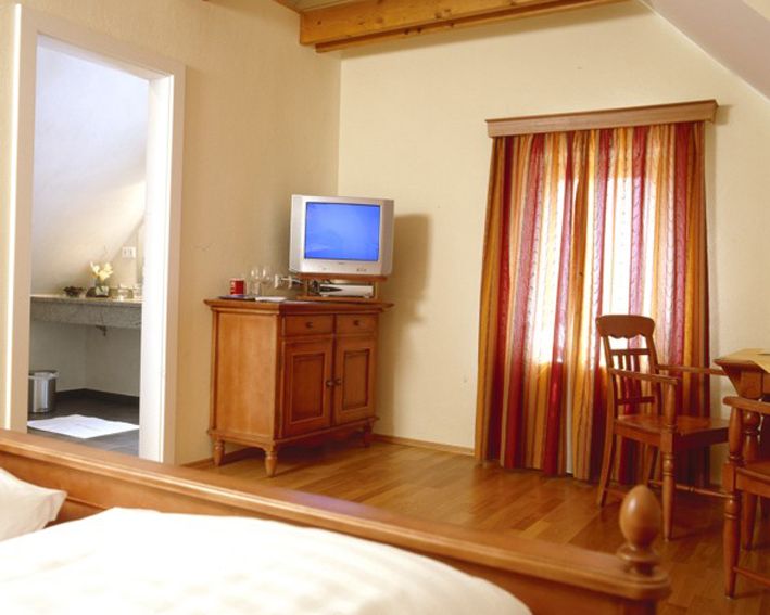 Gemütliches Zimmer mit Holzmöbeln, Fernseher und bunten Vorhängen.