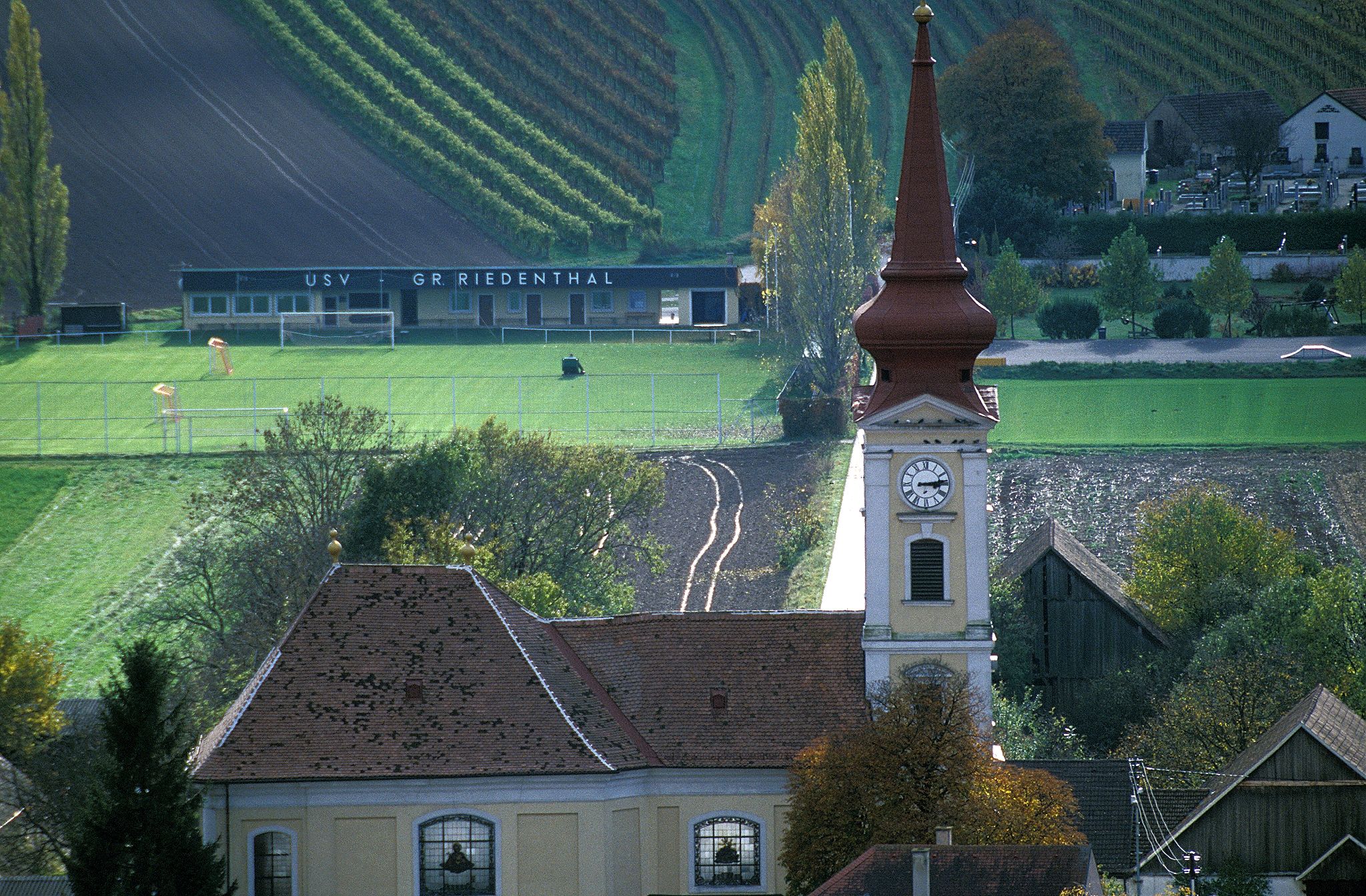 Pfarrkirche Großriedenthal mit Kirchturm und umliegenden Feldern und Gebäuden.