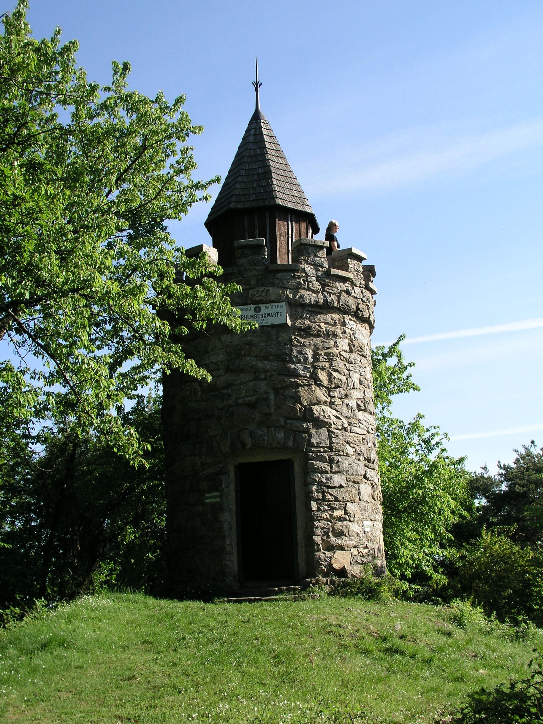 Steinerner Aussichtsturm mit spitzem Dach, umgeben von Bäumen, bei klarem Himmel.