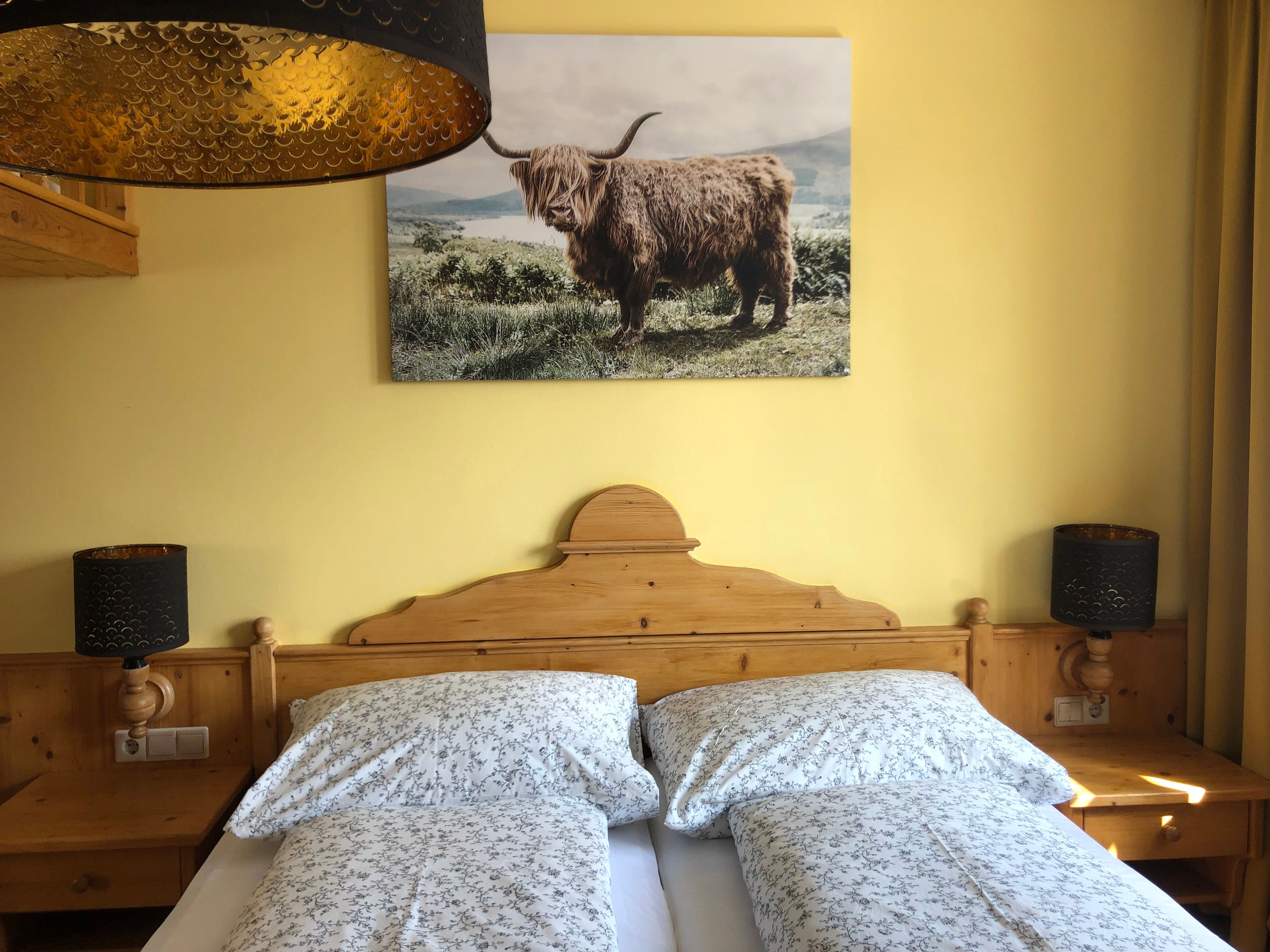Gemütliches Schlafzimmer mit Holzmöbeln, Doppelbett und Bild eines Hochlandrinds an der Wand.