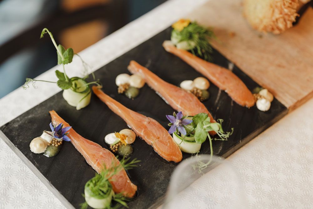 Gourmetgericht mit Lachs, Kräutern und Blüten auf Schieferplatte serviert.