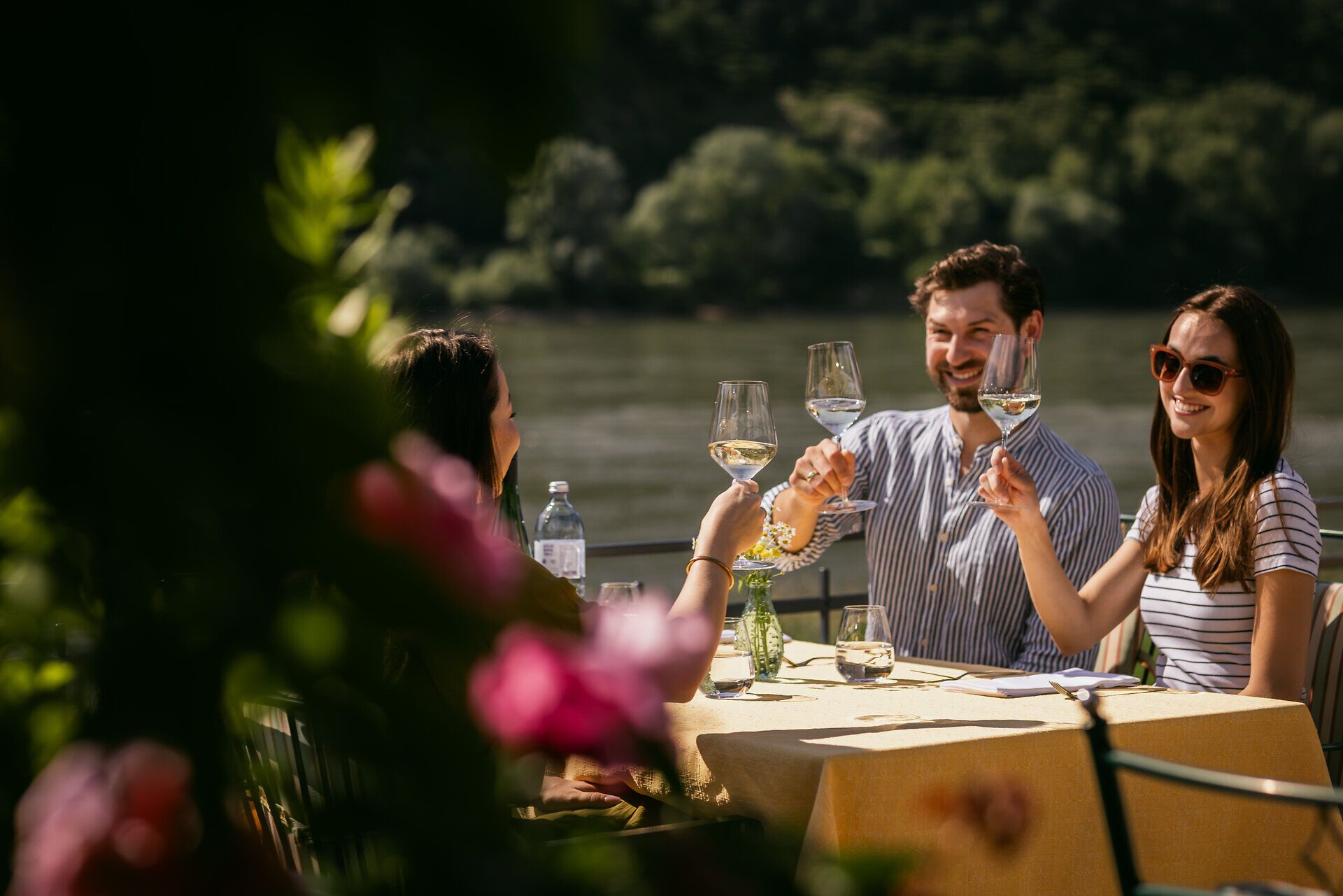 Drei Menschen sitzen an einem Tisch und prosten sich mit Weingläsern zu.