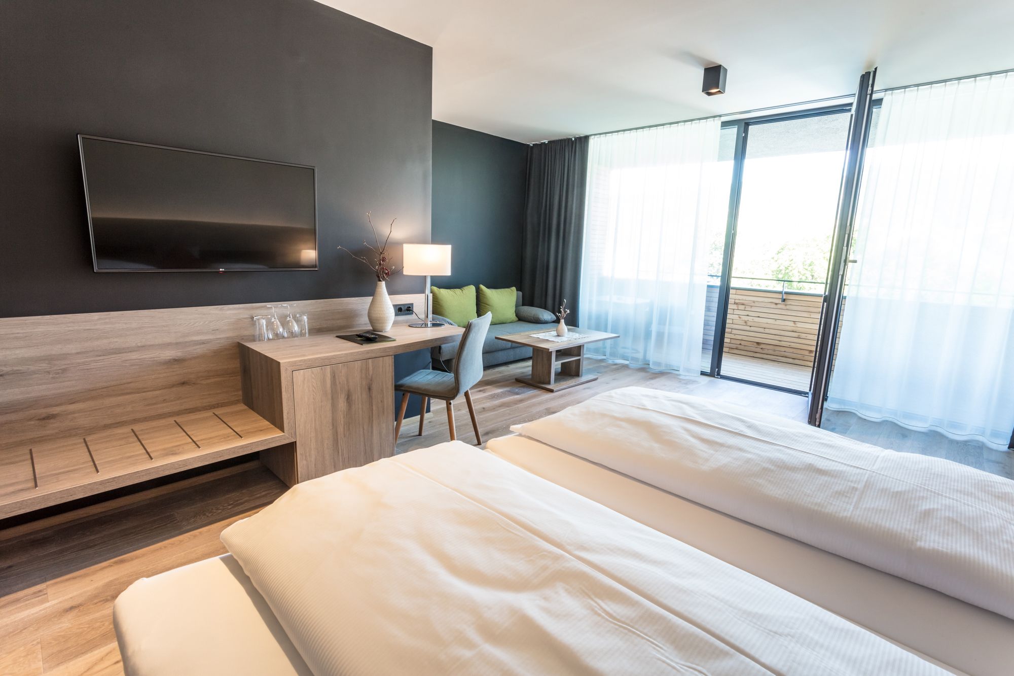 Modernes Hotelzimmer mit Doppelbett, Schreibtisch, Fernseher und Balkon.