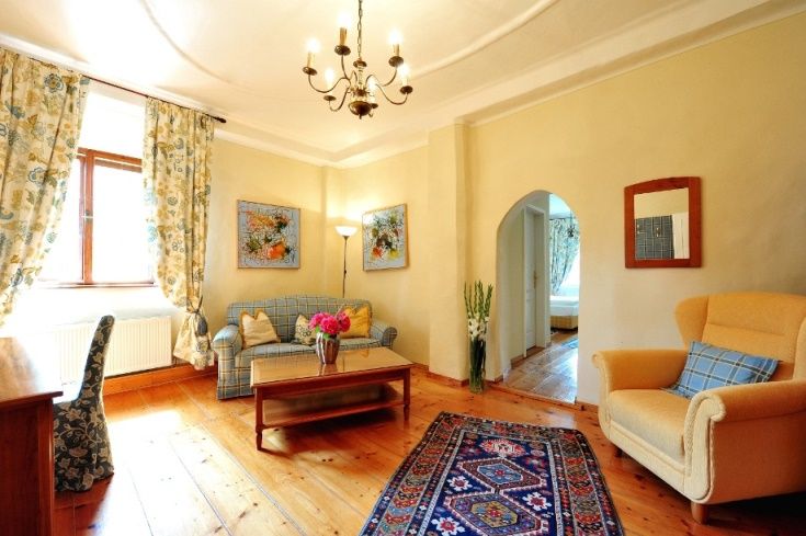 Gemütliches Wohnzimmer mit Holzboden, Sofa, Sessel, Teppich und Blumen.