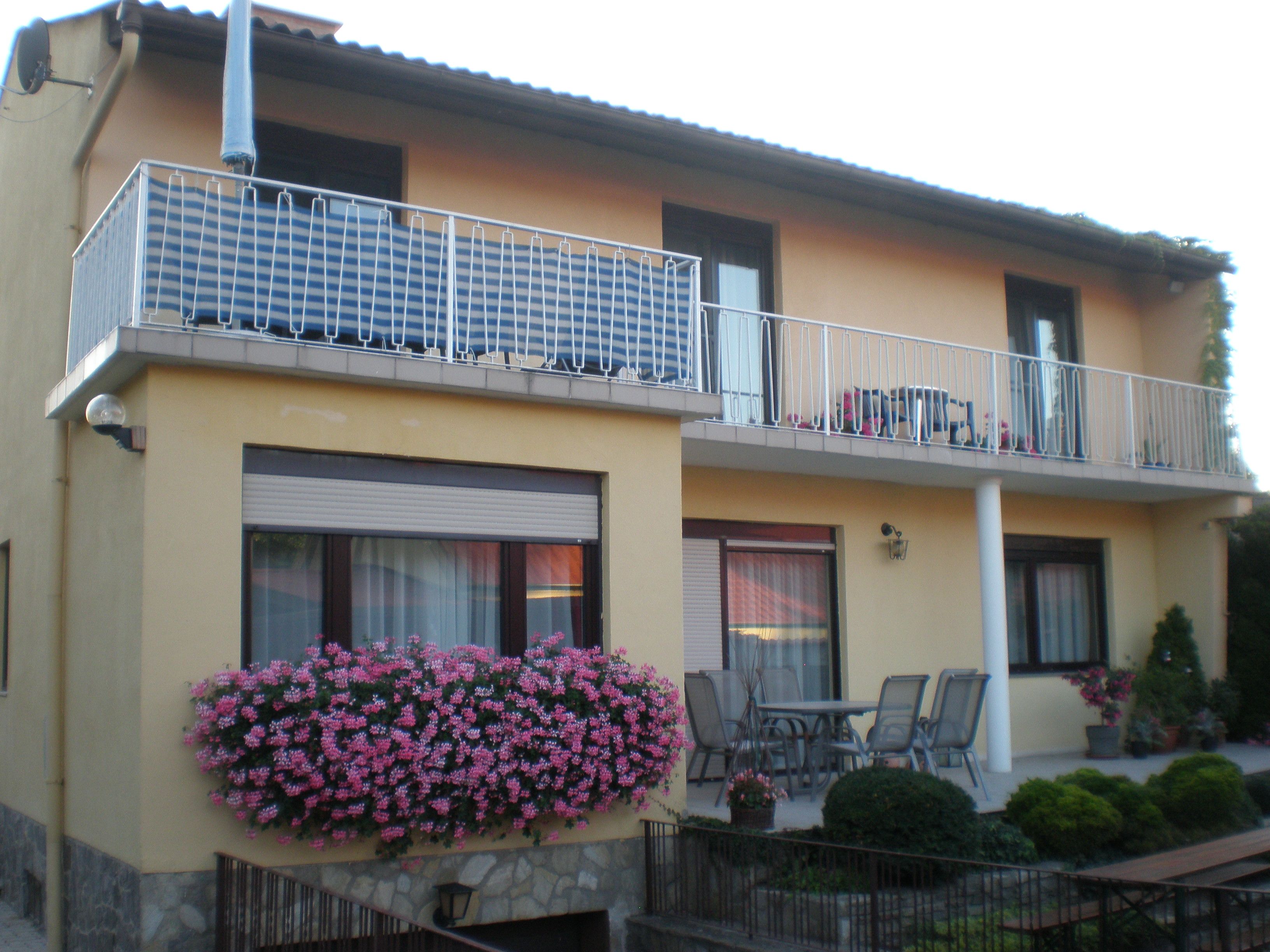 Zweistöckiges Haus mit Balkon, Blumen und Gartenmöbeln.