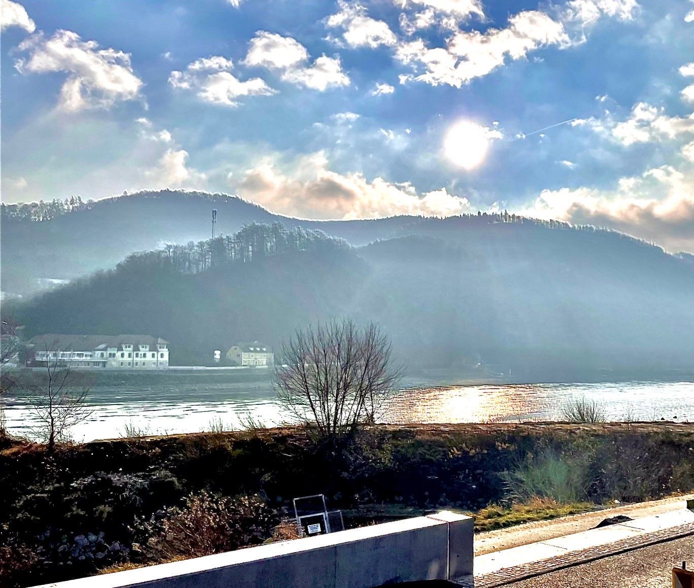 Sonnenstrahlen über einem Fluss mit Hügeln im Hintergrund.