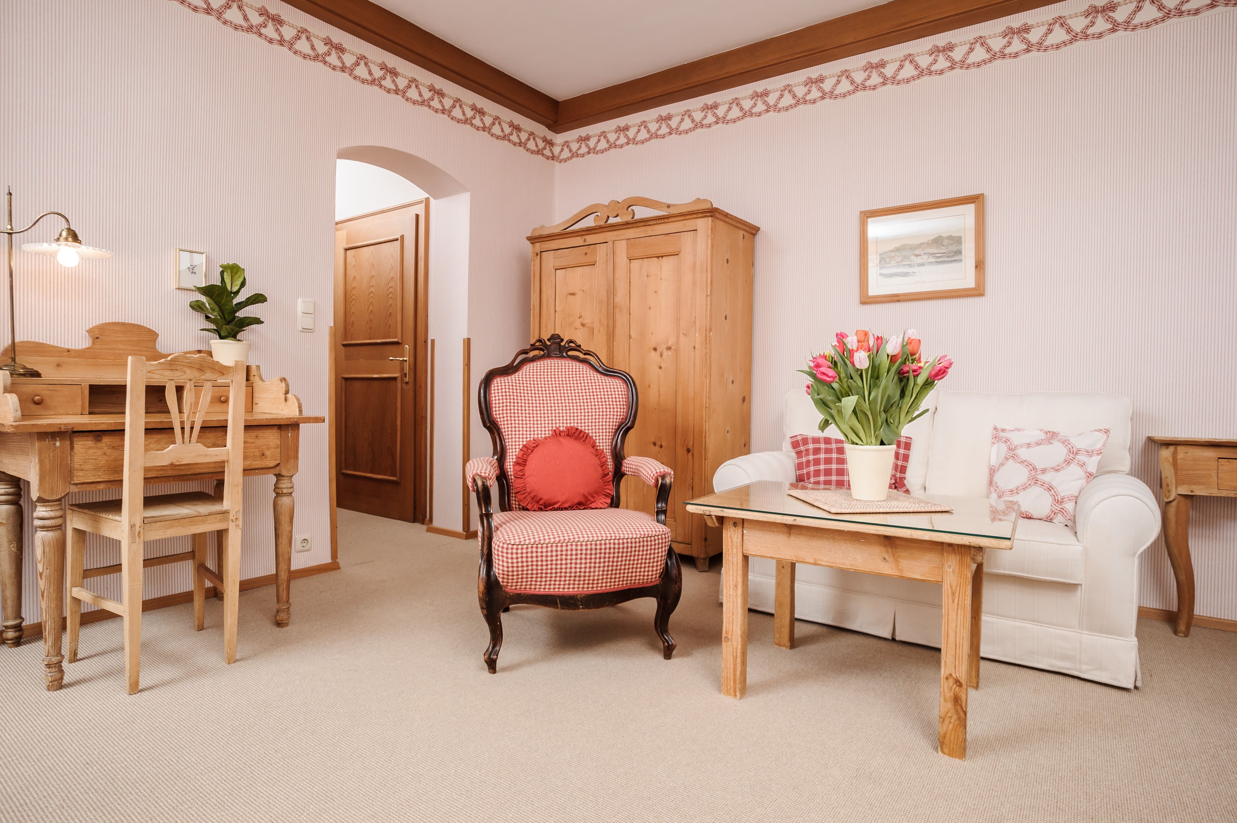 Gemütliches Wohnzimmer mit Holzmöbeln, einem Sessel, Sofa und Tisch mit Tulpen.