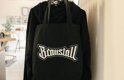 Schwarze Tasche mit Braustall-Logo vor schwarzer Kleidung.