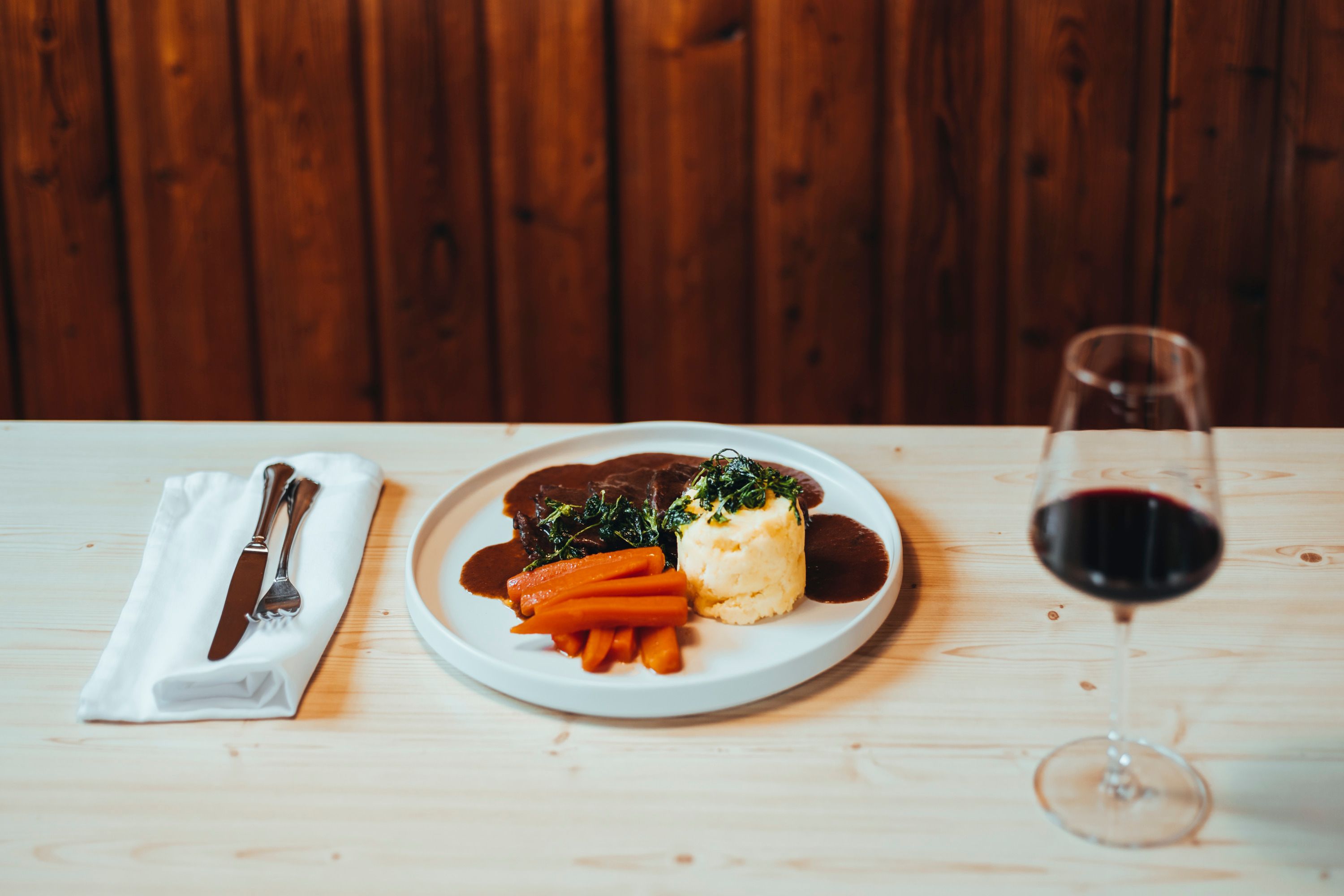 Elegantes Gericht mit Fleisch, Gemüse und Rotwein auf Holztisch.