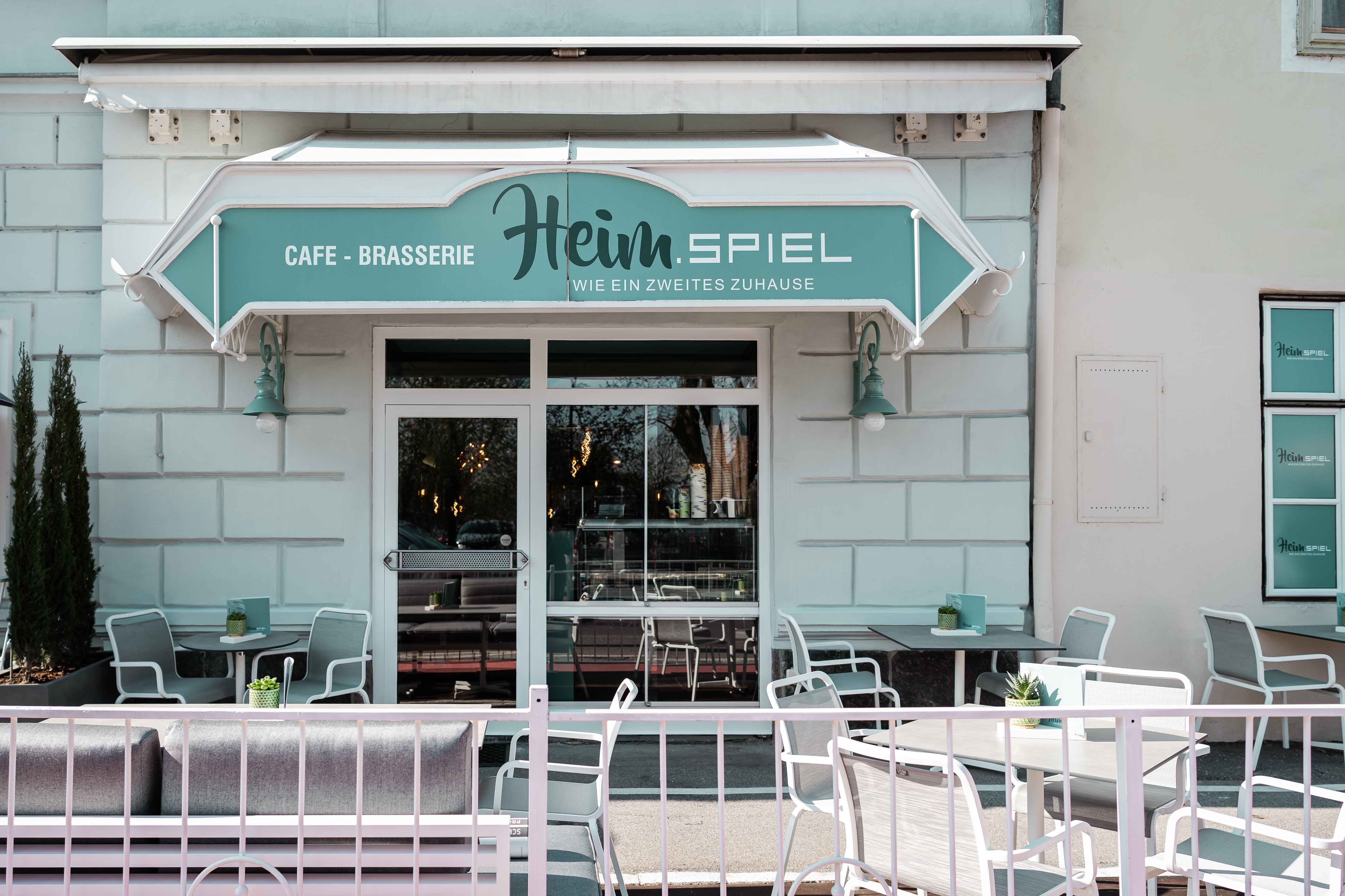 Außenansicht eines Cafés mit Terrasse und Sitzgelegenheiten.