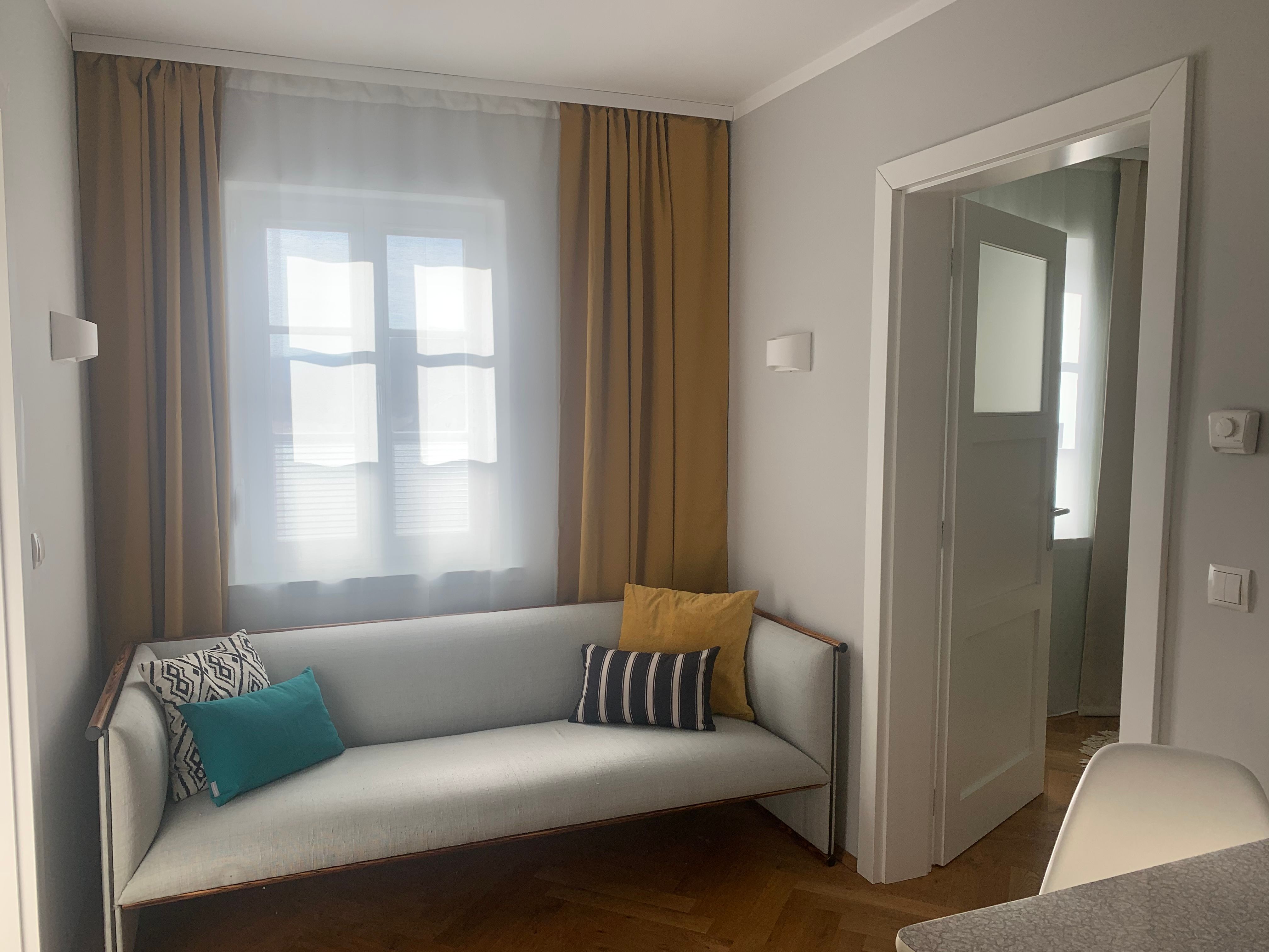 Gemütliches Wohnzimmer mit Sofa und Kissen, gelben Vorhängen und offenem Türrahmen.