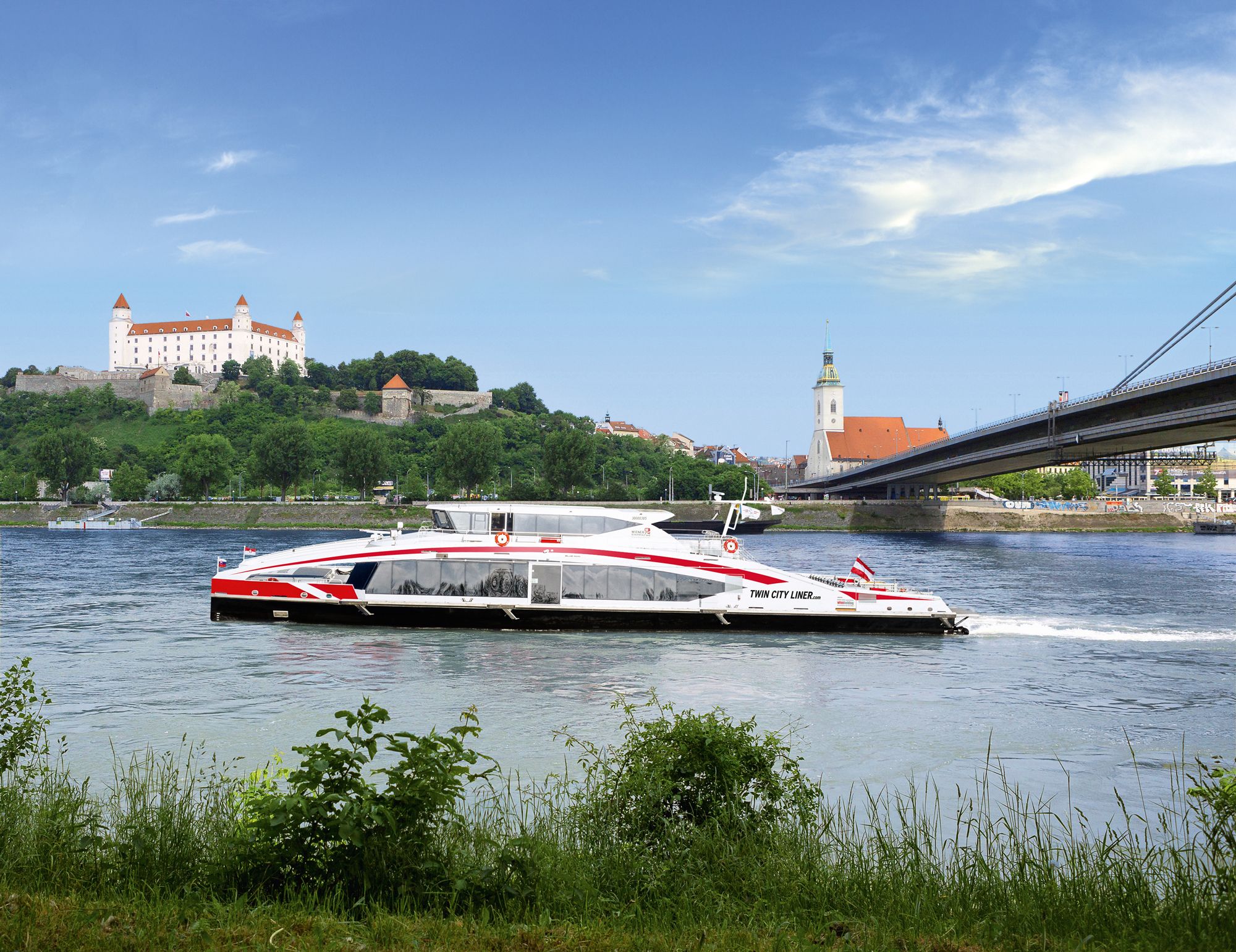 TwinSchiff auf dem Wasser und im Hintergrund die Burg Bratislava und eine Brücke