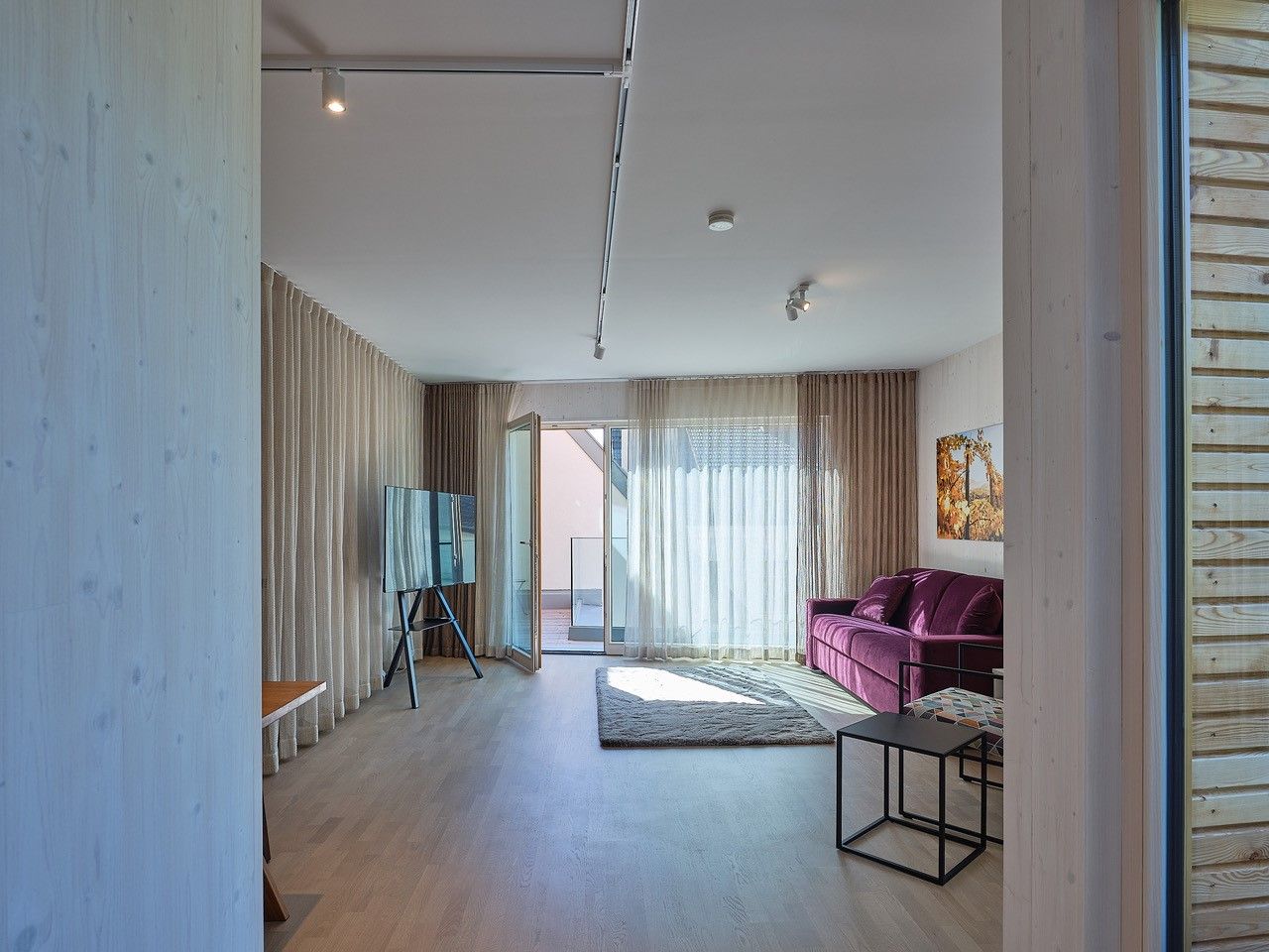 Modernes Wohnzimmer mit lila Sofa, großem Fenster und TV auf Ständer.