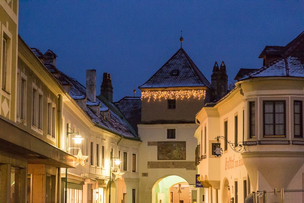 Eine malerische Altstadtgasse im Winter mit festlicher Beleuchtung und schneebedeckten Dächern.