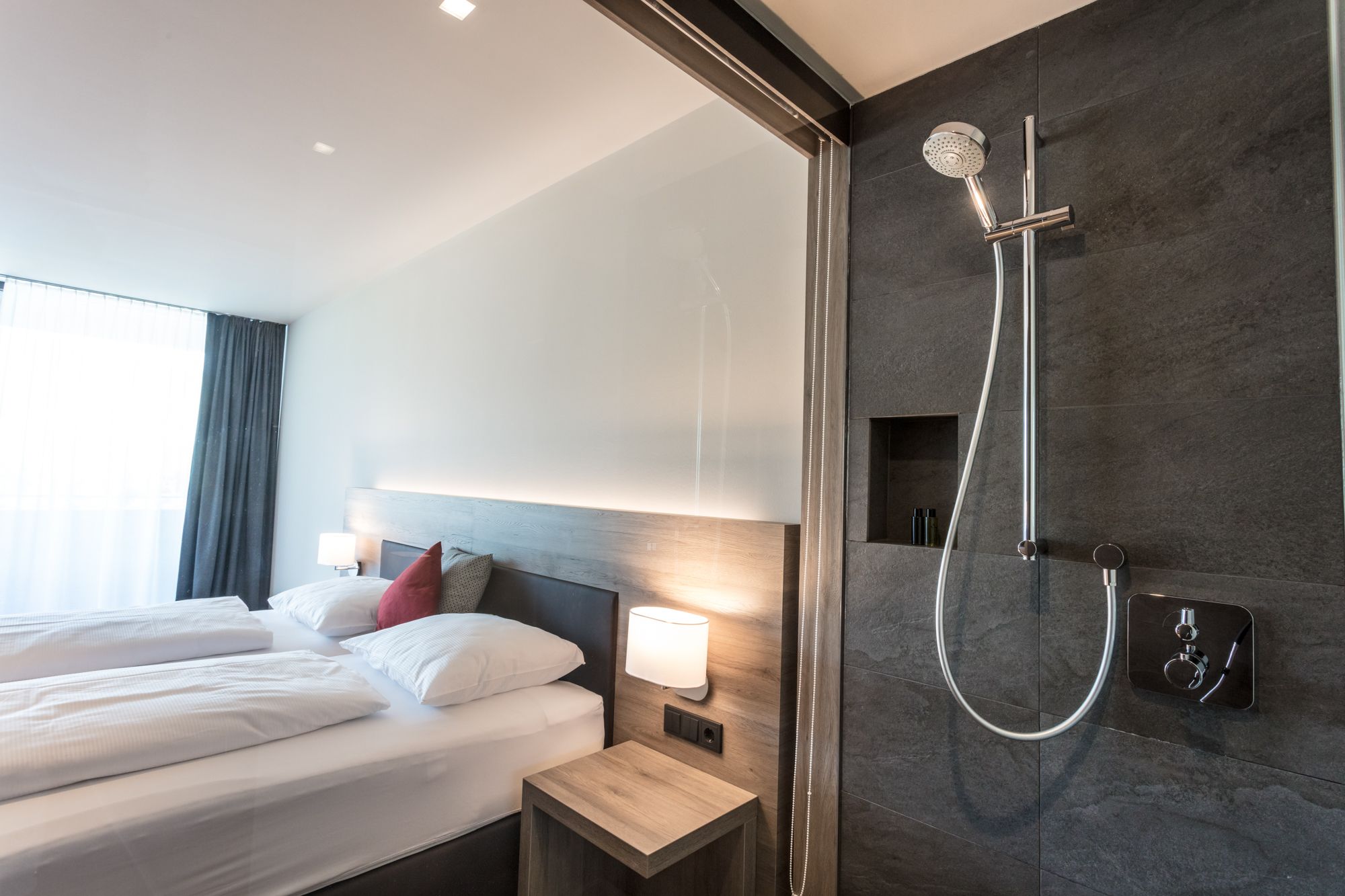 Modernes Hotelzimmer mit Doppelbett und offener Dusche.