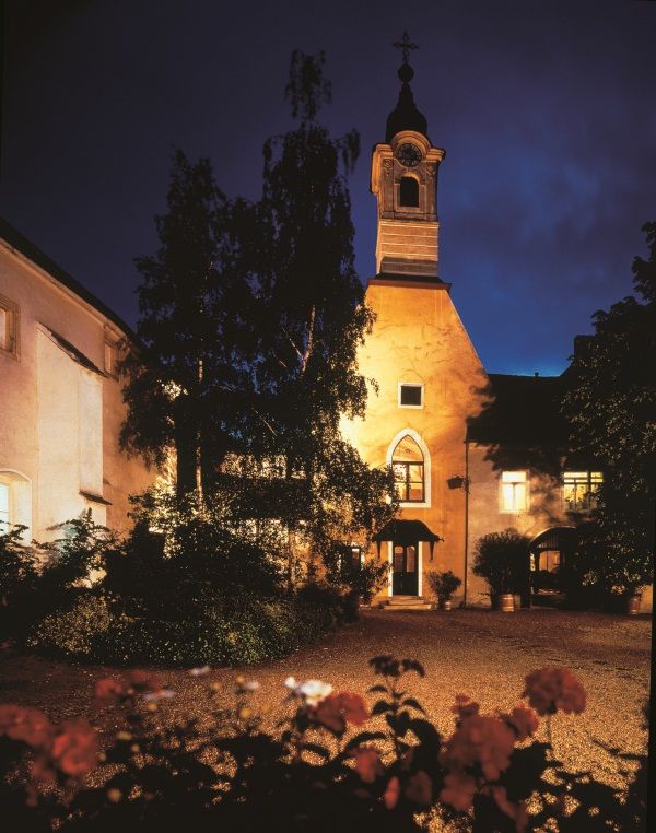 Beleuchtetes Gebäude bei Nacht mit Turm und Bäumen im Vordergrund.