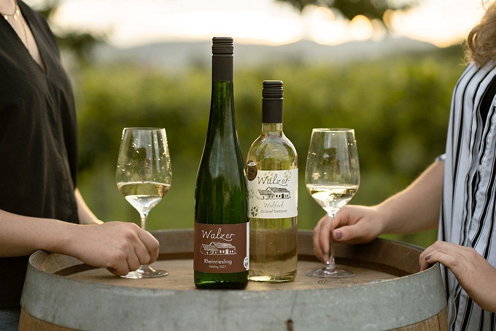 Two wine bottles and glasses on a wine barrel outdoors.